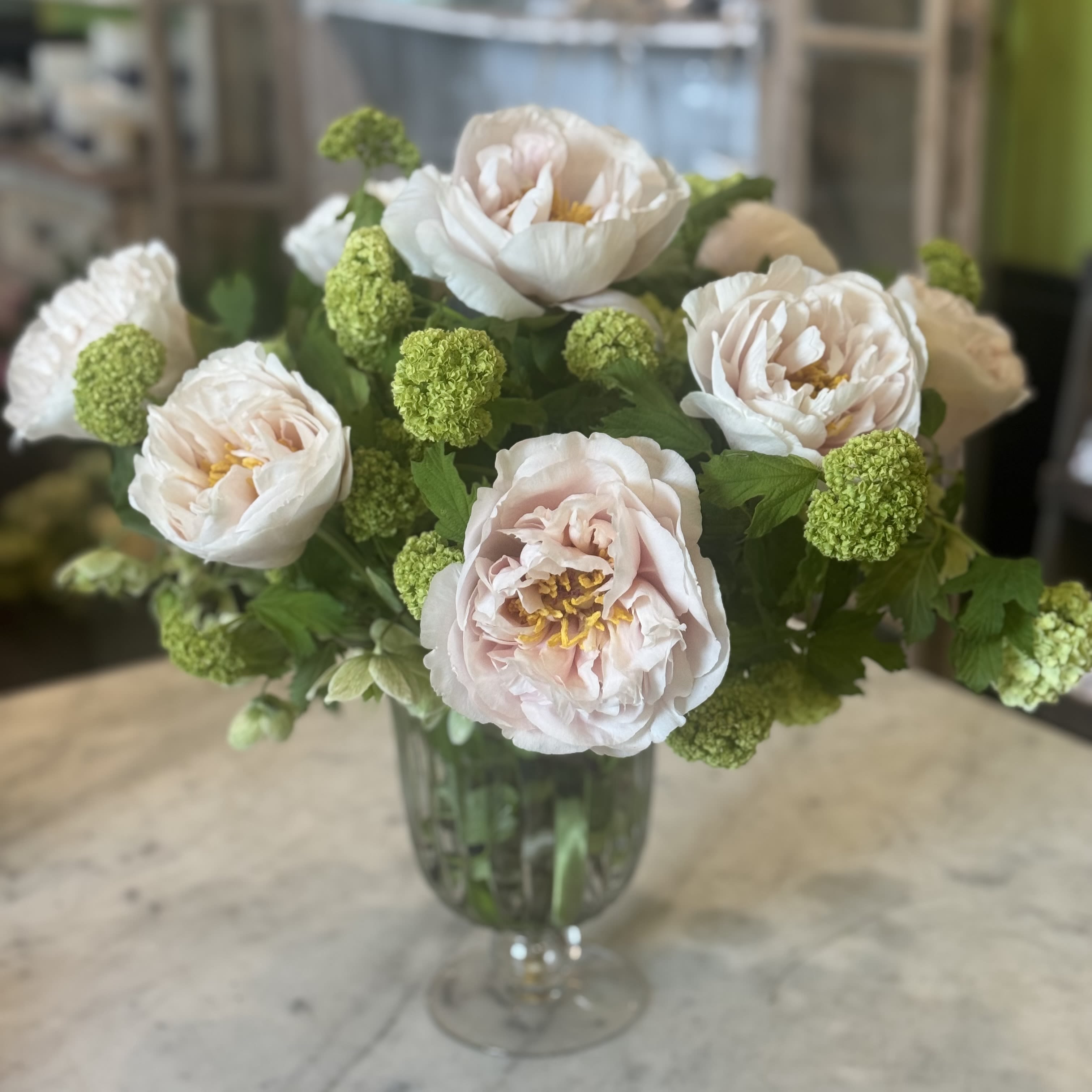 Urban Gardener Blushing Princess Peony  - Two dozen Antonia Garden roses loosely arranged in a footed glass urn.
