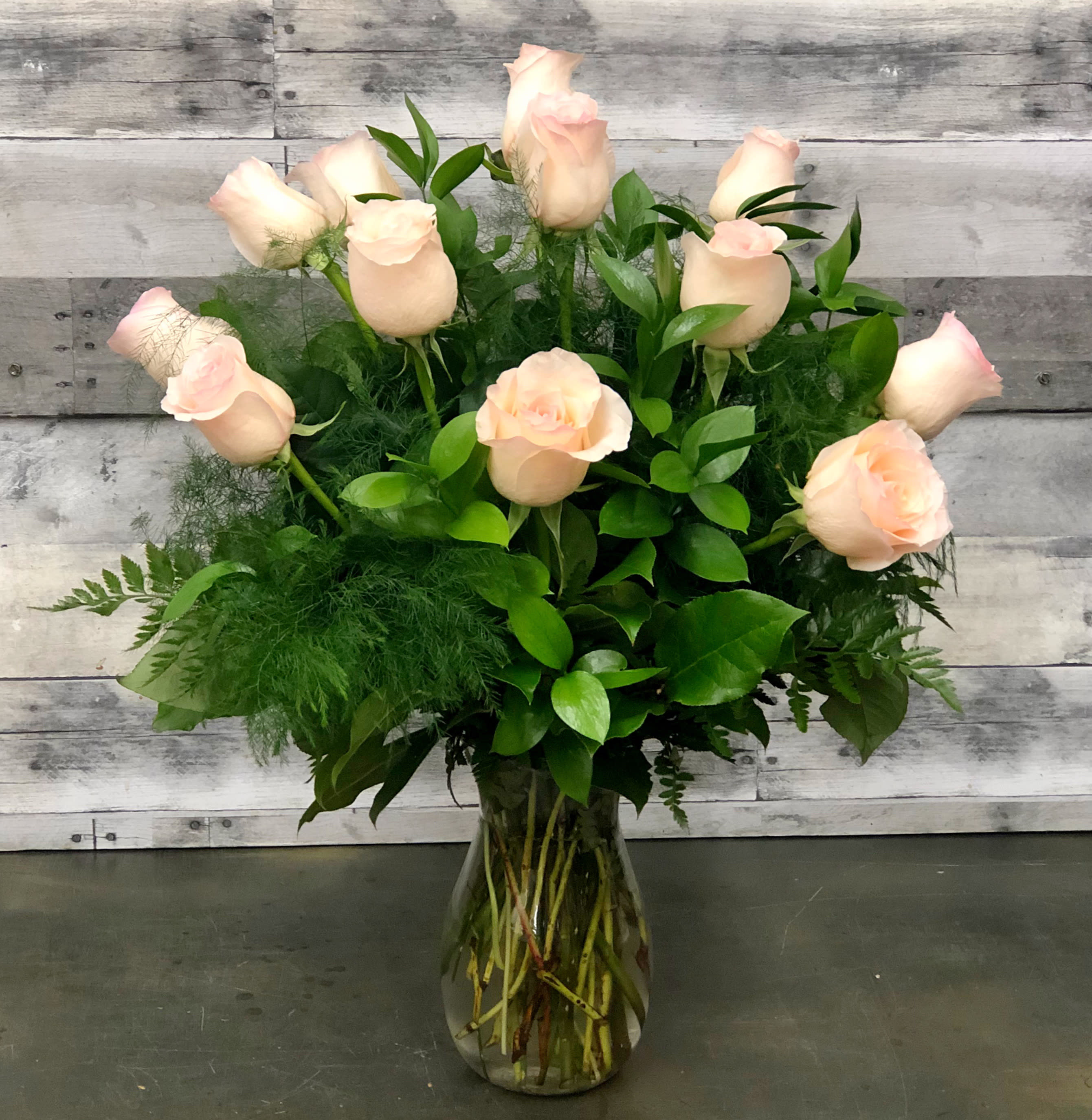 Pale pink roses arranged in a clear glass vase with lush greenery