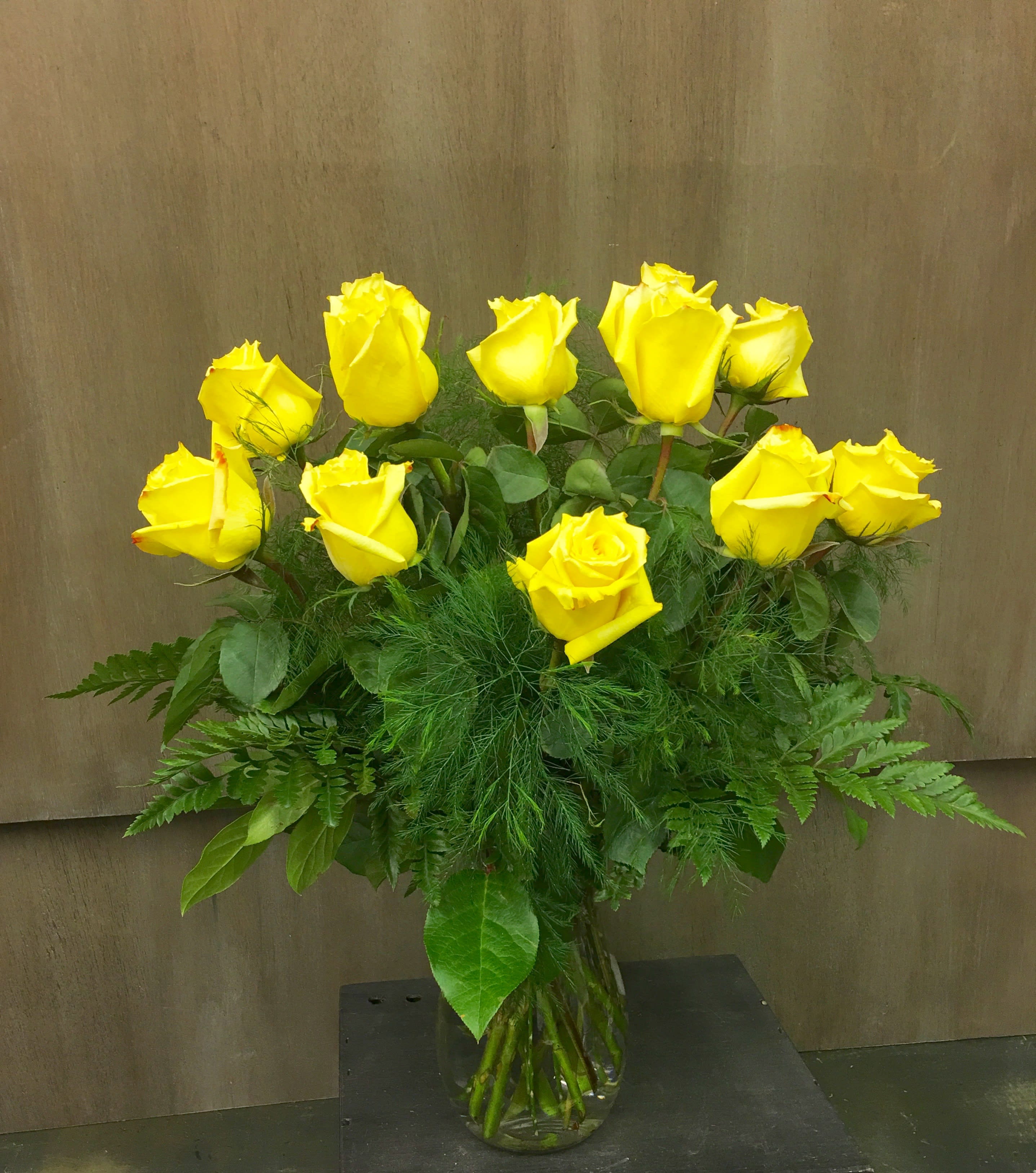 Yellow roses arranged in a clear glass vase with lush greenery