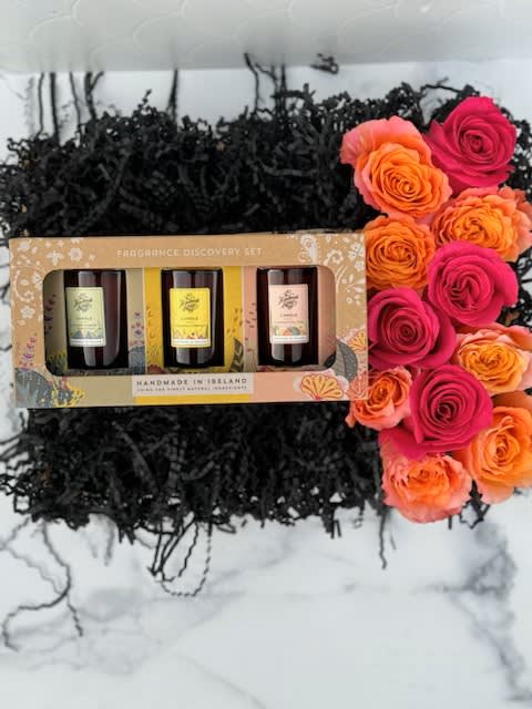 Boxed candle gift set on black shred with a row of pink and orange roses on the side