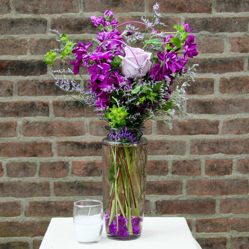 Purple floral arrangement in a tall glass vase with a white rose