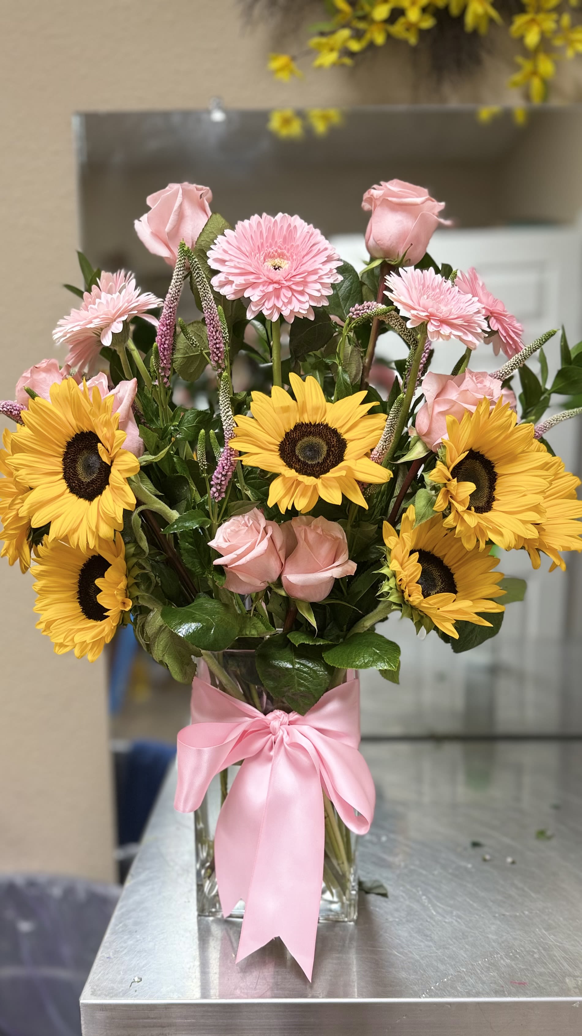 Bouquet of pink roses and yellow sunflowers in a clear vase with a pink ribbon