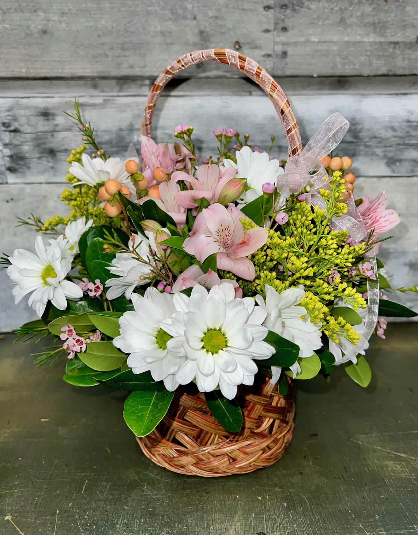 Basket arrangement of white daisies and pink lilies with a ribbon bow