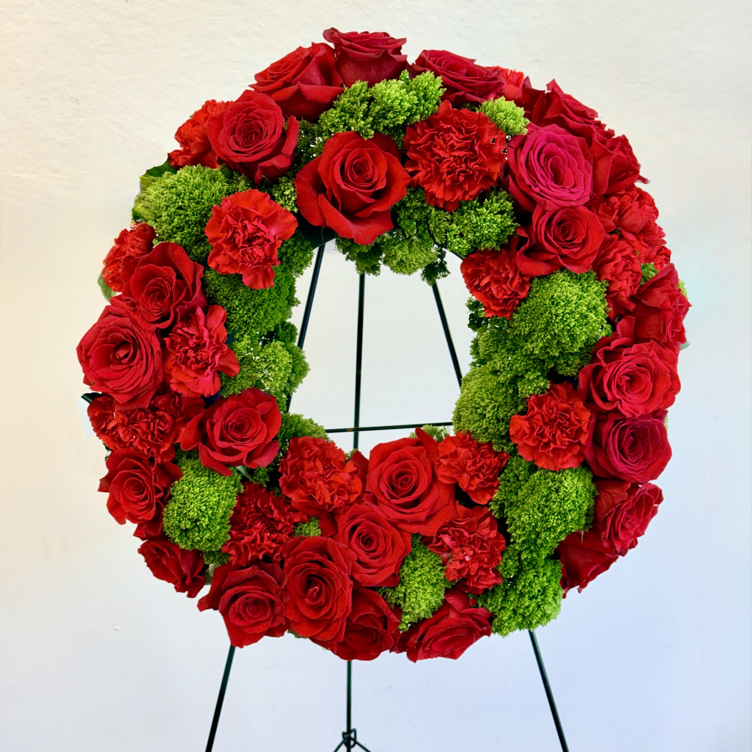 Red and Green Wreath - A graceful sympathy wreath of rich red roses and carnations accented with vibrant green hydrangea, symbolizing deep love, remembrance, and enduring devotion. A heartfelt expression of respect and compassion for honoring a cherished life.