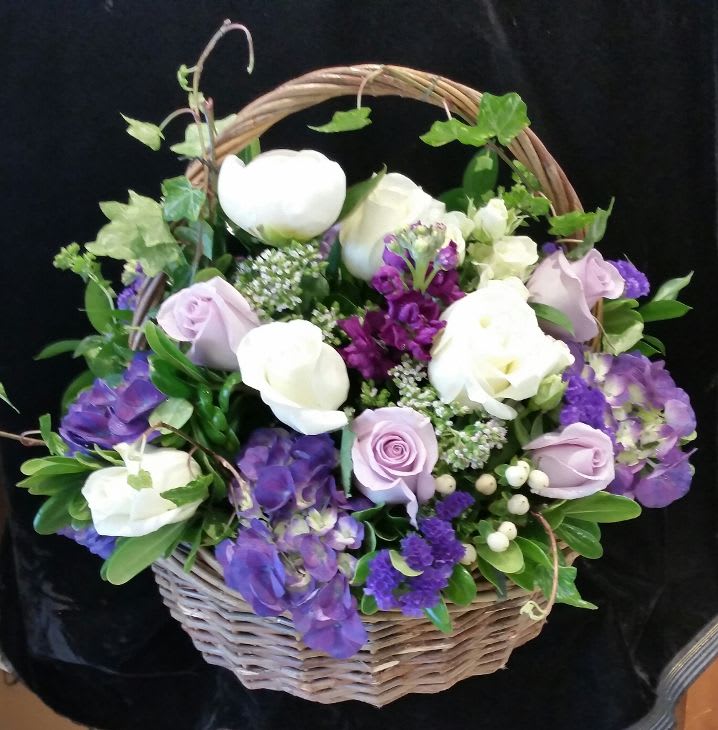 Basket arrangement of white and lavender roses with purple flowers