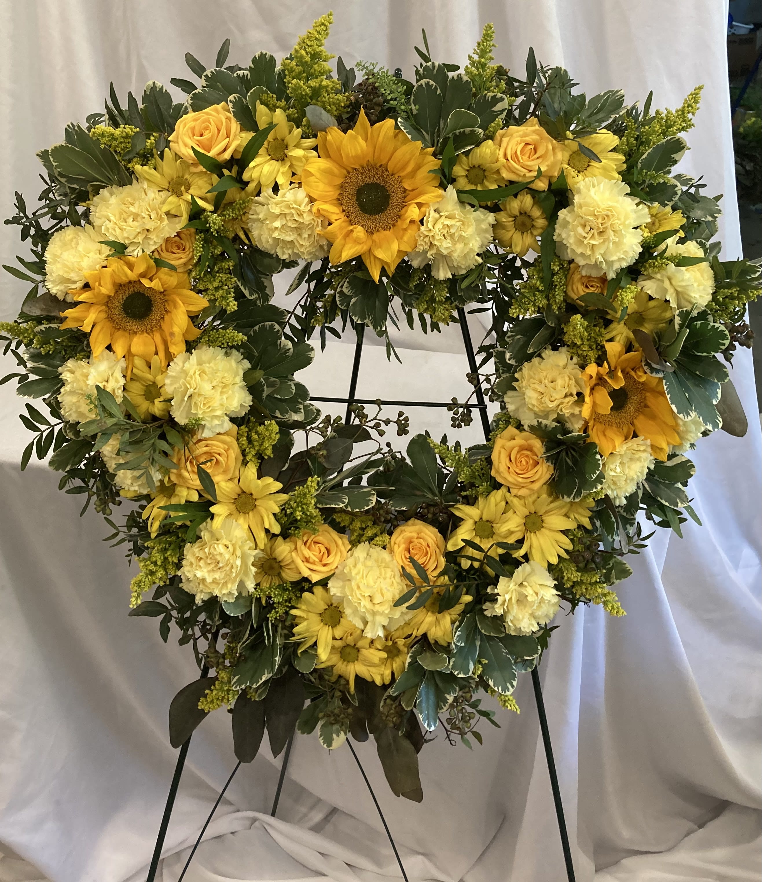 Heart-shaped floral wreath with yellow flowers on a black stand