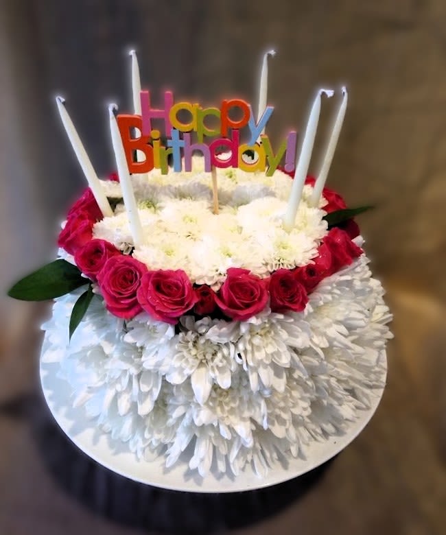 Round cake-shaped arrangement of white mums and pink roses with tall candles and a Happy Birthday pick