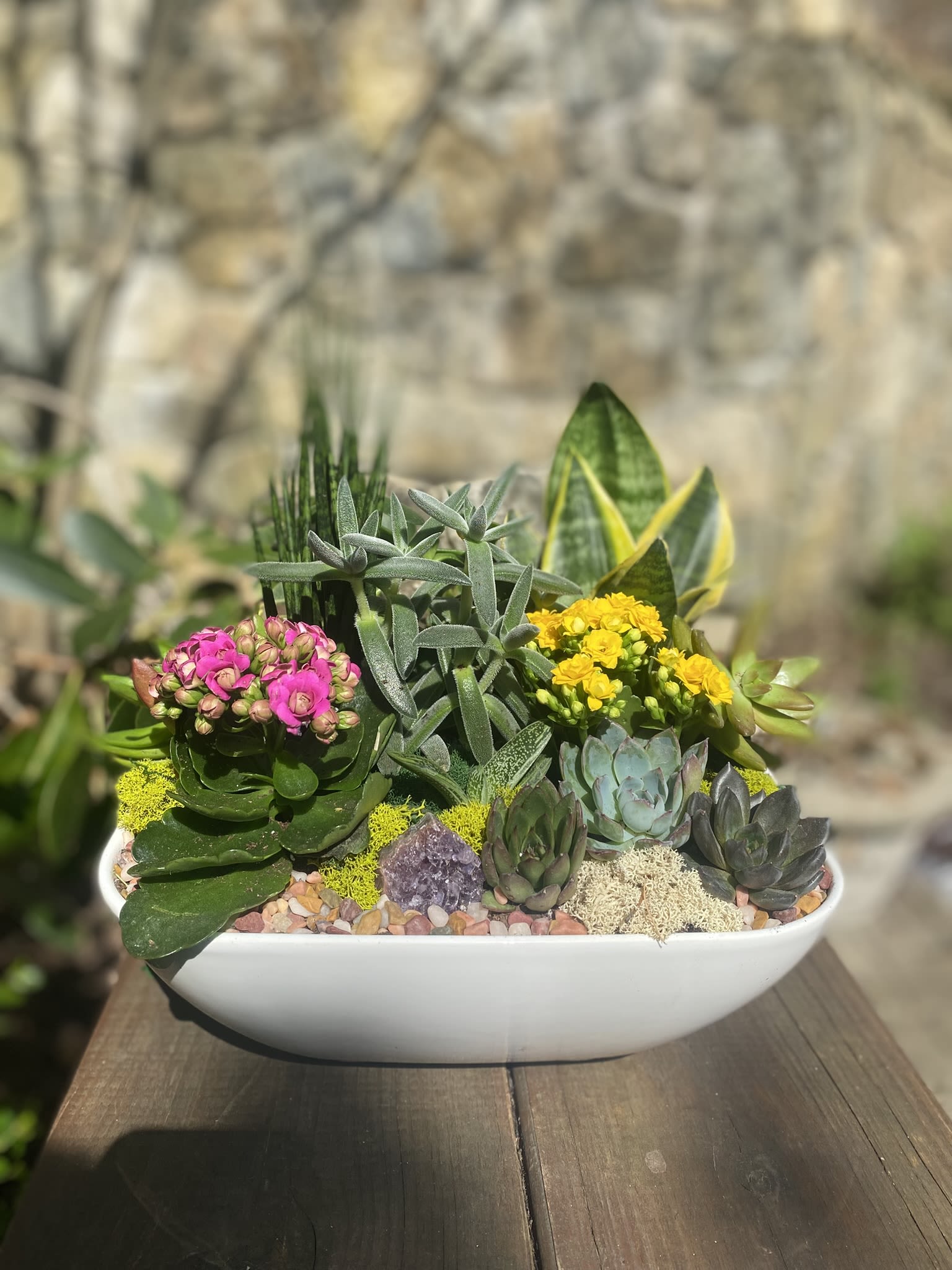 Succulent arrangement with pink and yellow blooms in a white bowl planter