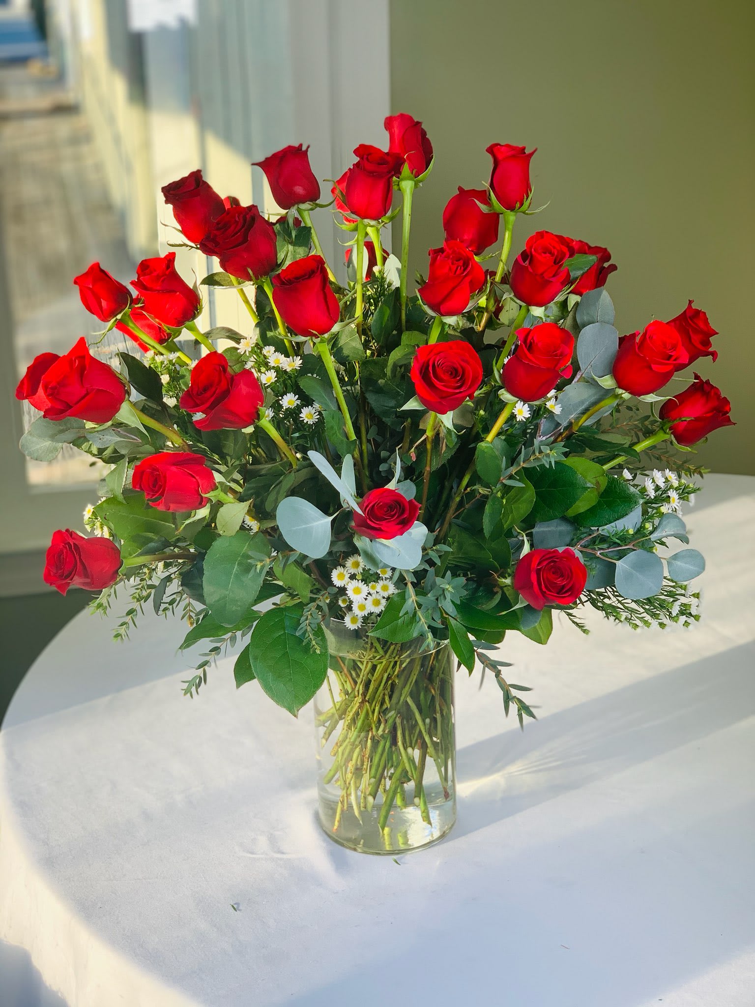 Red roses arranged in a clear glass vase with small white filler flowers