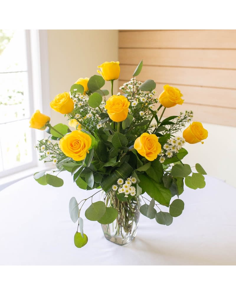 Yellow roses in a clear glass vase with small white filler flowers