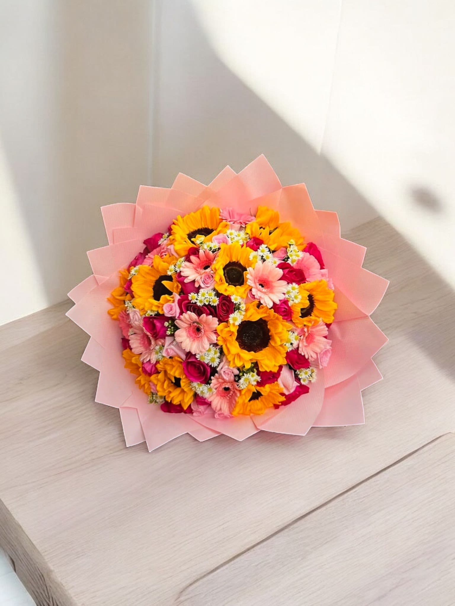 Pink-wrapped bouquet of sunflowers, gerbera daisies, and roses