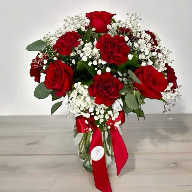Red roses and carnations in a glass vase with baby's breath and a red ribbon