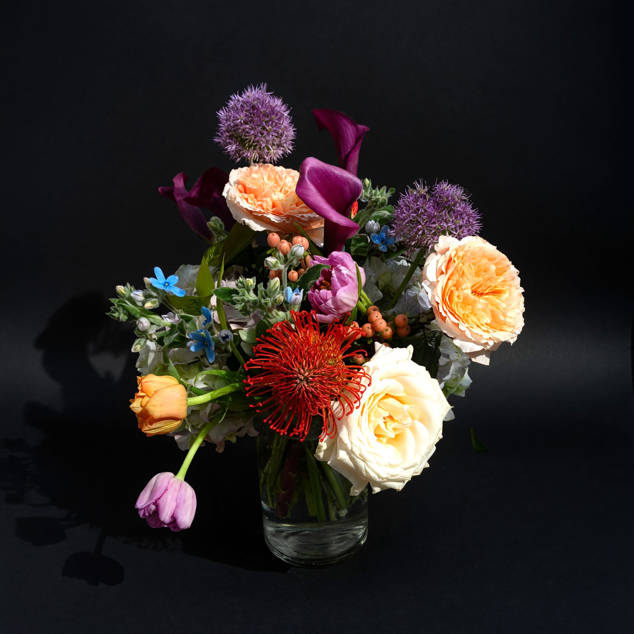 Genevieve - Peach roses and deep purple calla lilies create a modern, eye-catching mix in this mixed-color flower arrangement-perfect as a Mother's Day bouquet or a cheerful "thinking of you" gift. The composition balances rounded, soft blooms with taller, sculptural elements so the person you're sending it to will feel noticed and celebrated the moment it arrives.