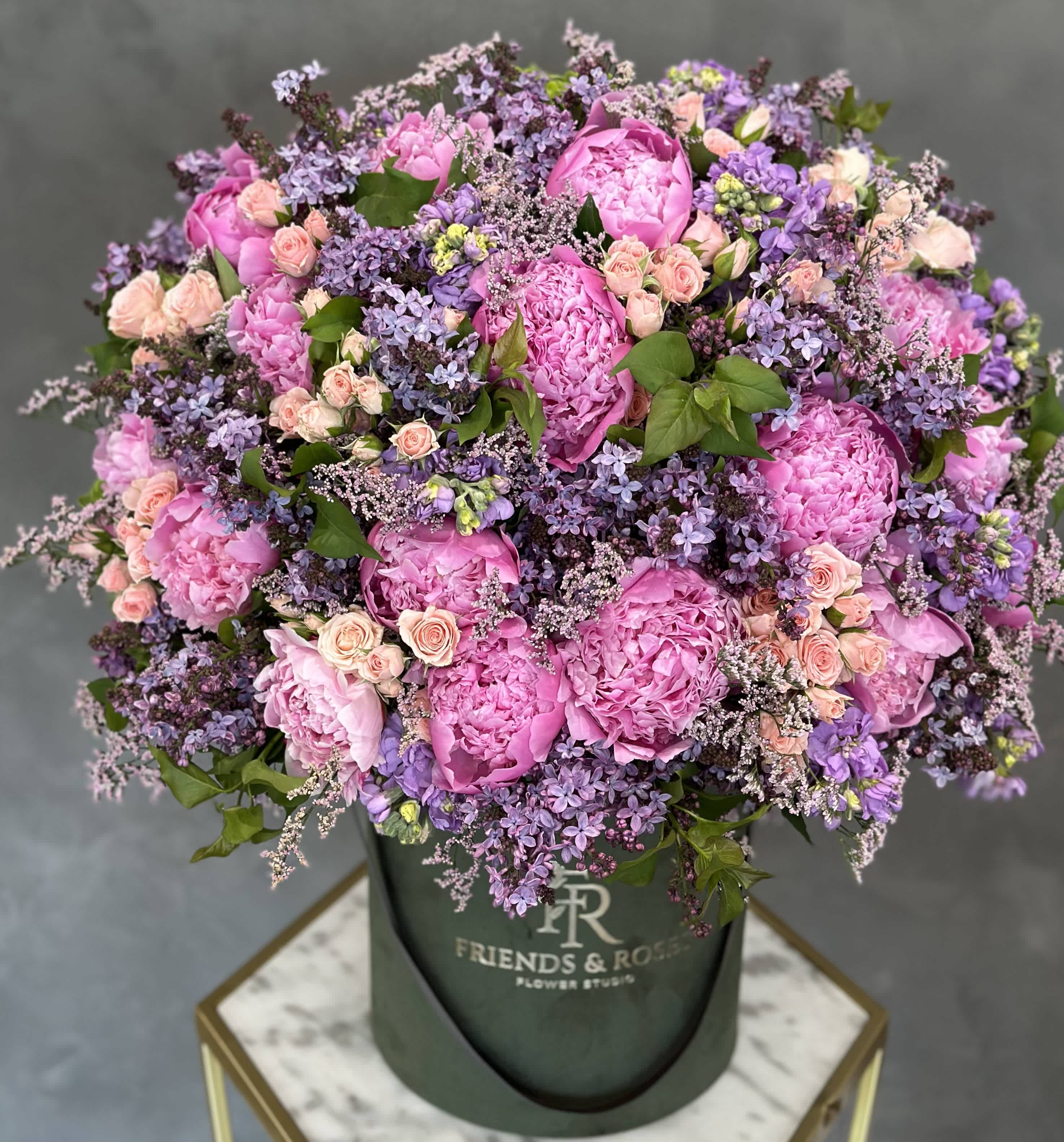 Pink peonies and lavender flowers in a dark green hat box