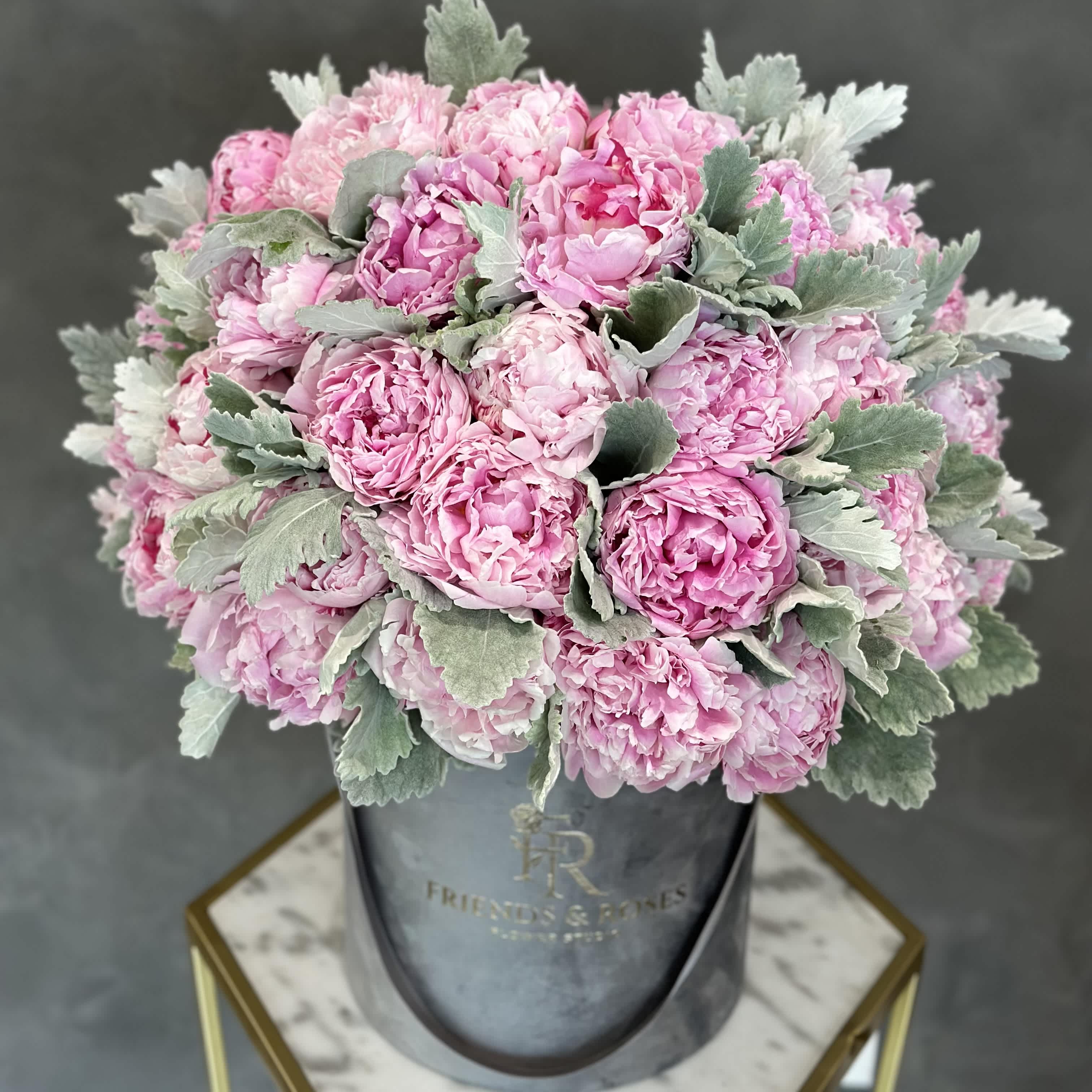 Pink peony bouquet in a gray hatbox with silvery foliage