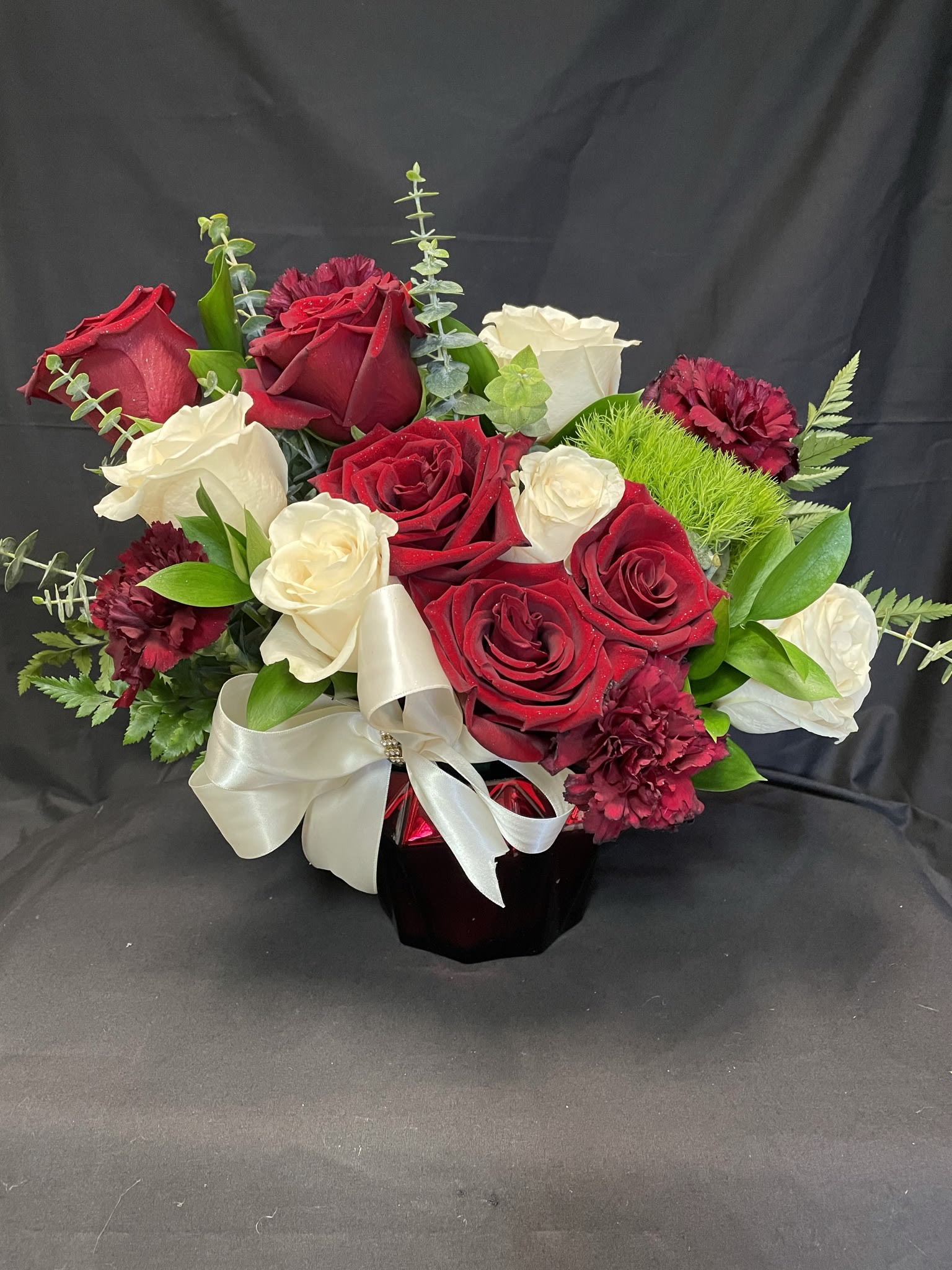 Red and white rose bouquet in a dark vase with a white ribbon