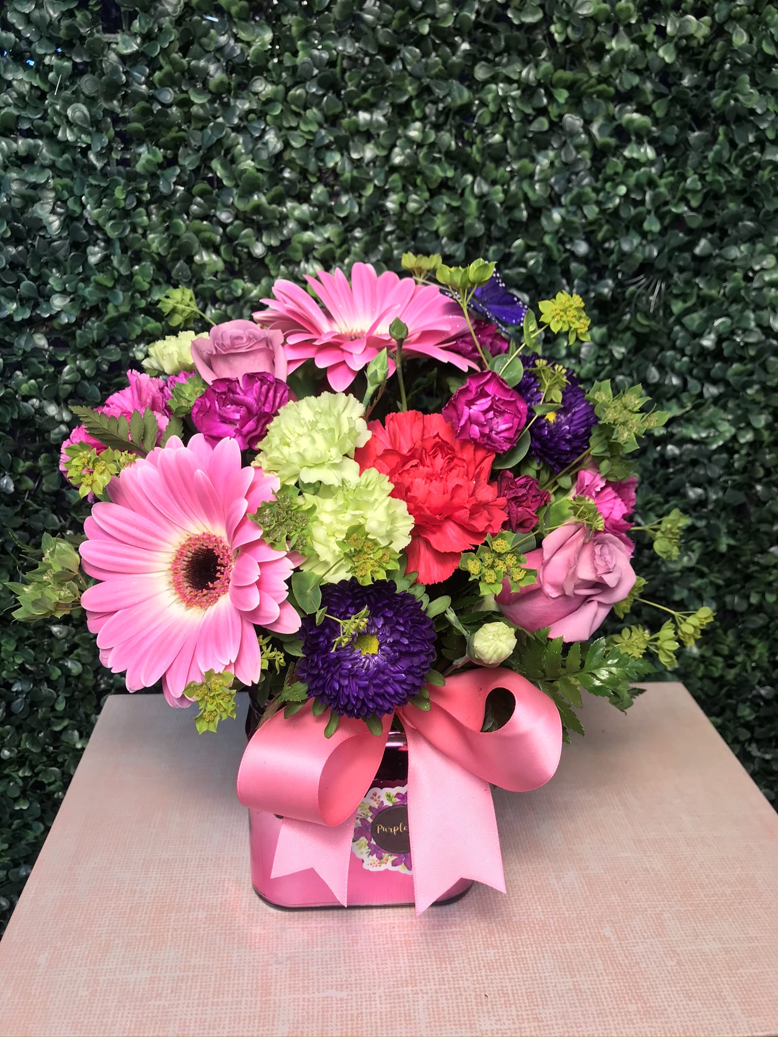 Pink and purple mixed flower arrangement in a pink box with a ribbon