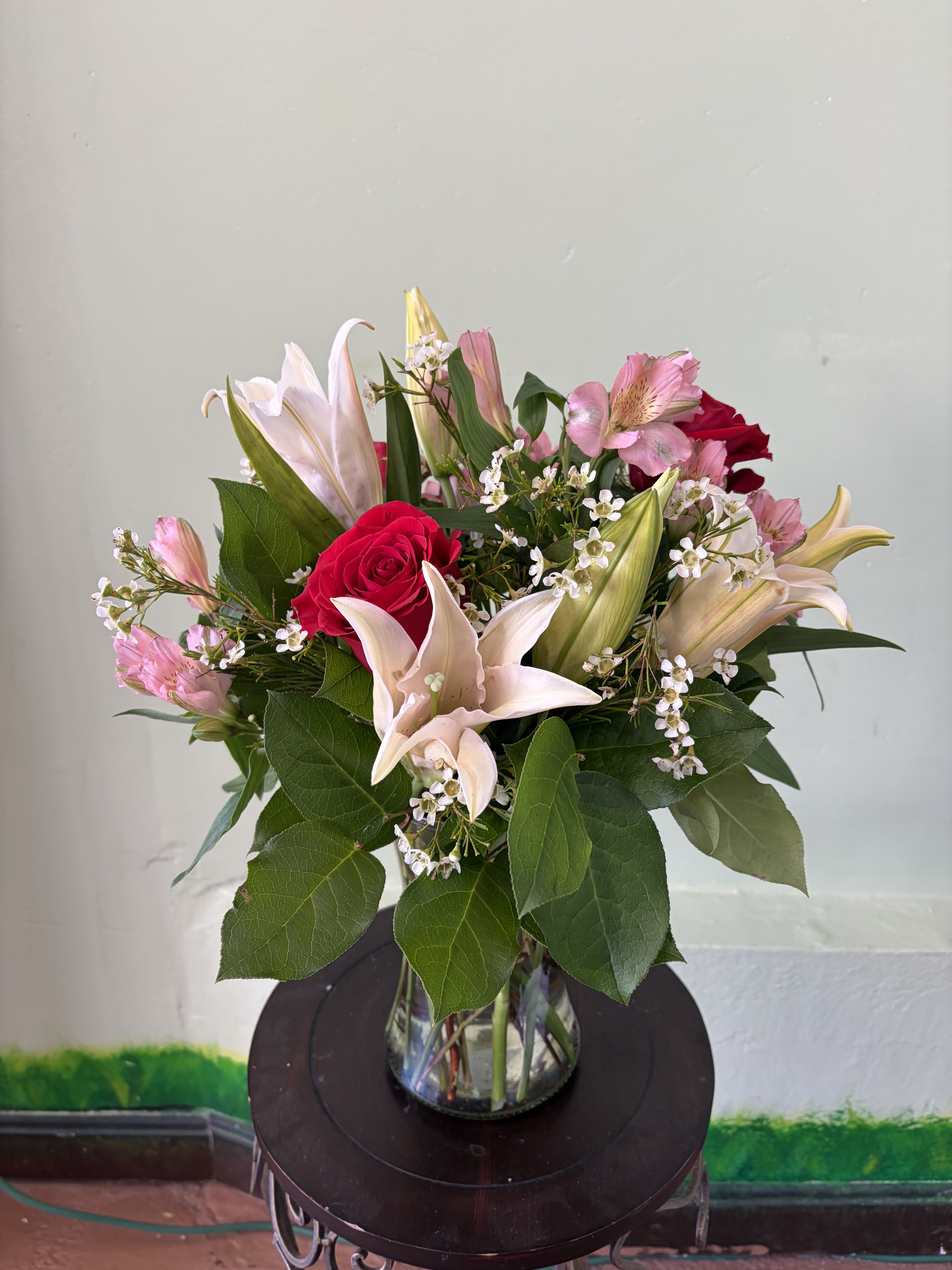 Morning Blush Garden - A graceful arrangement with soft pastel tones, rich accents, and fresh greenery arranged in a clear vase. The gentle color contrast and natural flow create an elegant, balanced look that brightens any space and makes a thoughtful gift for many occasions.