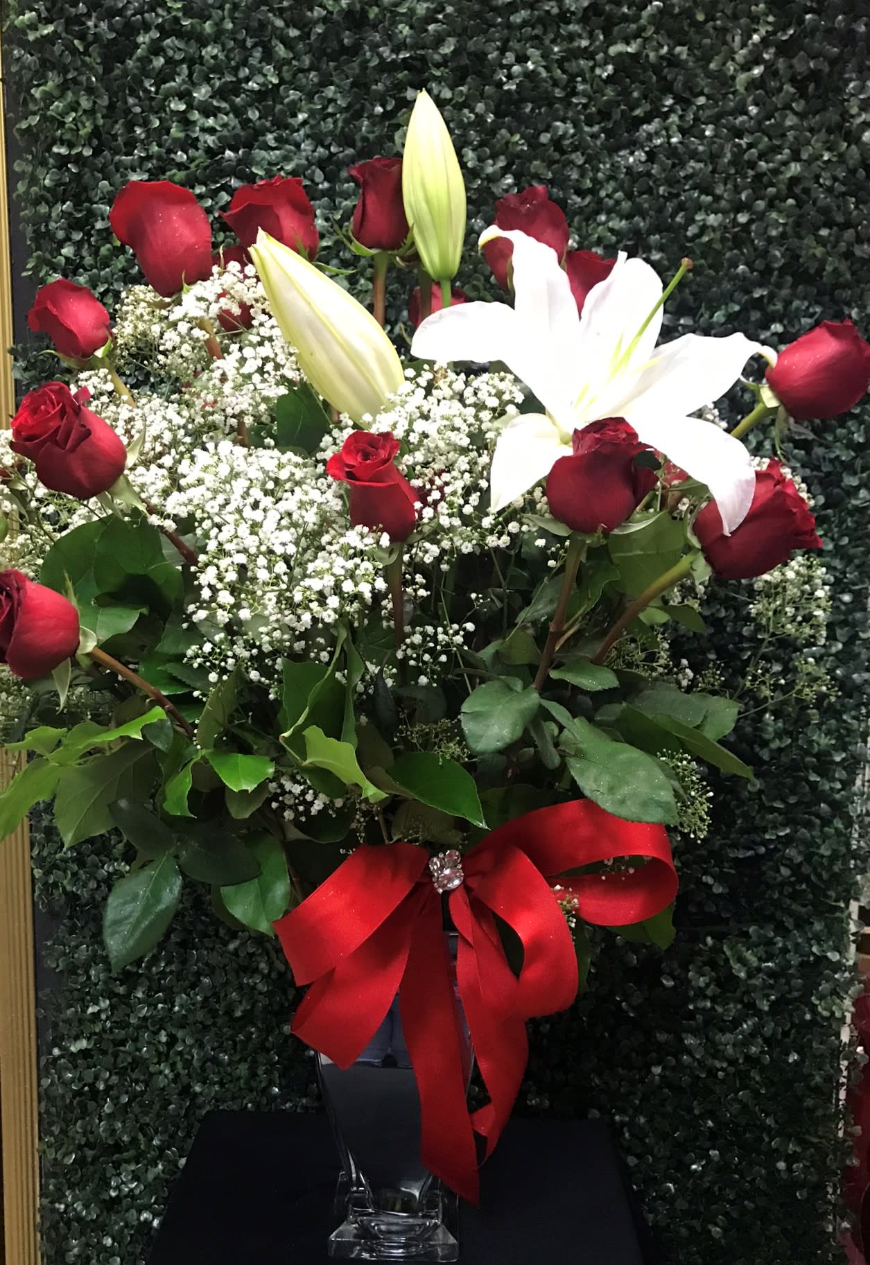 Red roses and white lilies in a clear vase with a red ribbon