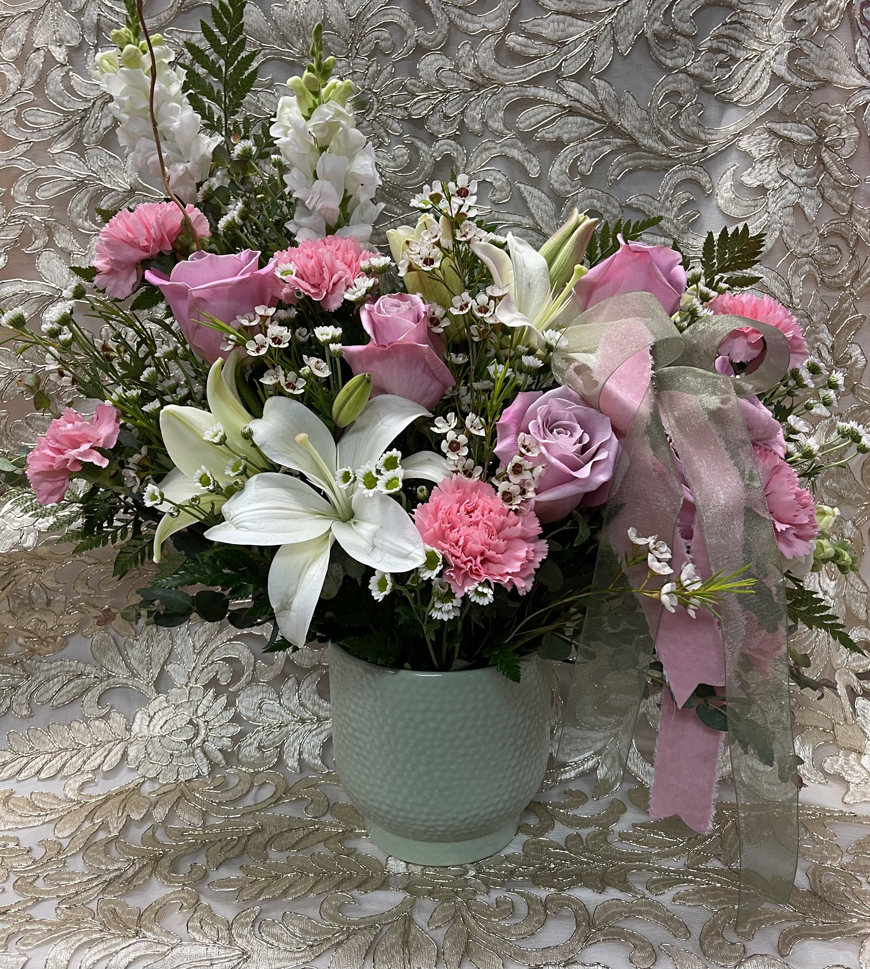 Pink and white floral arrangement in a pale green vase with a ribbon bow
