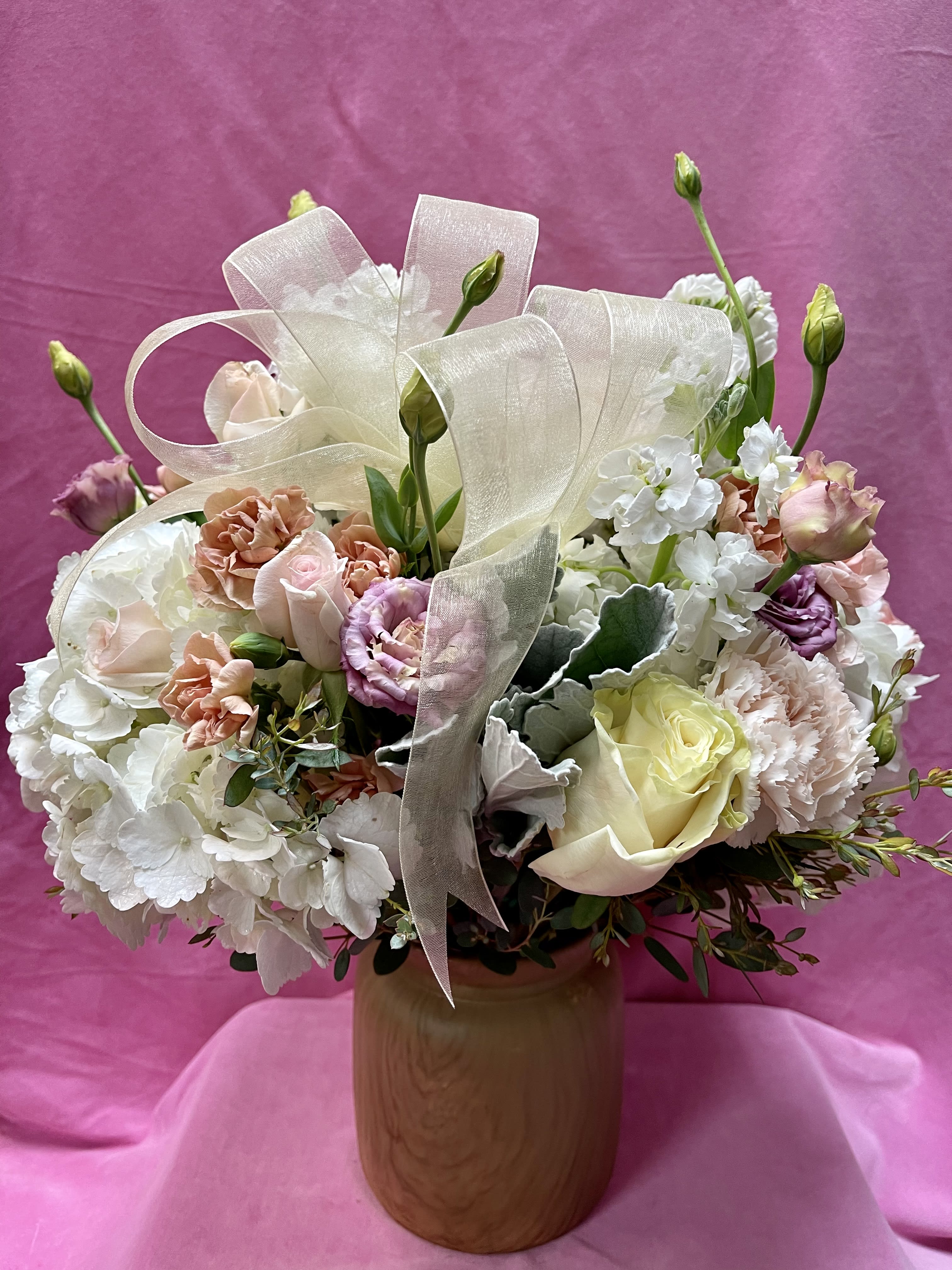 Pastel bouquet of roses, carnations, and white blooms in a wooden vase with ribbon