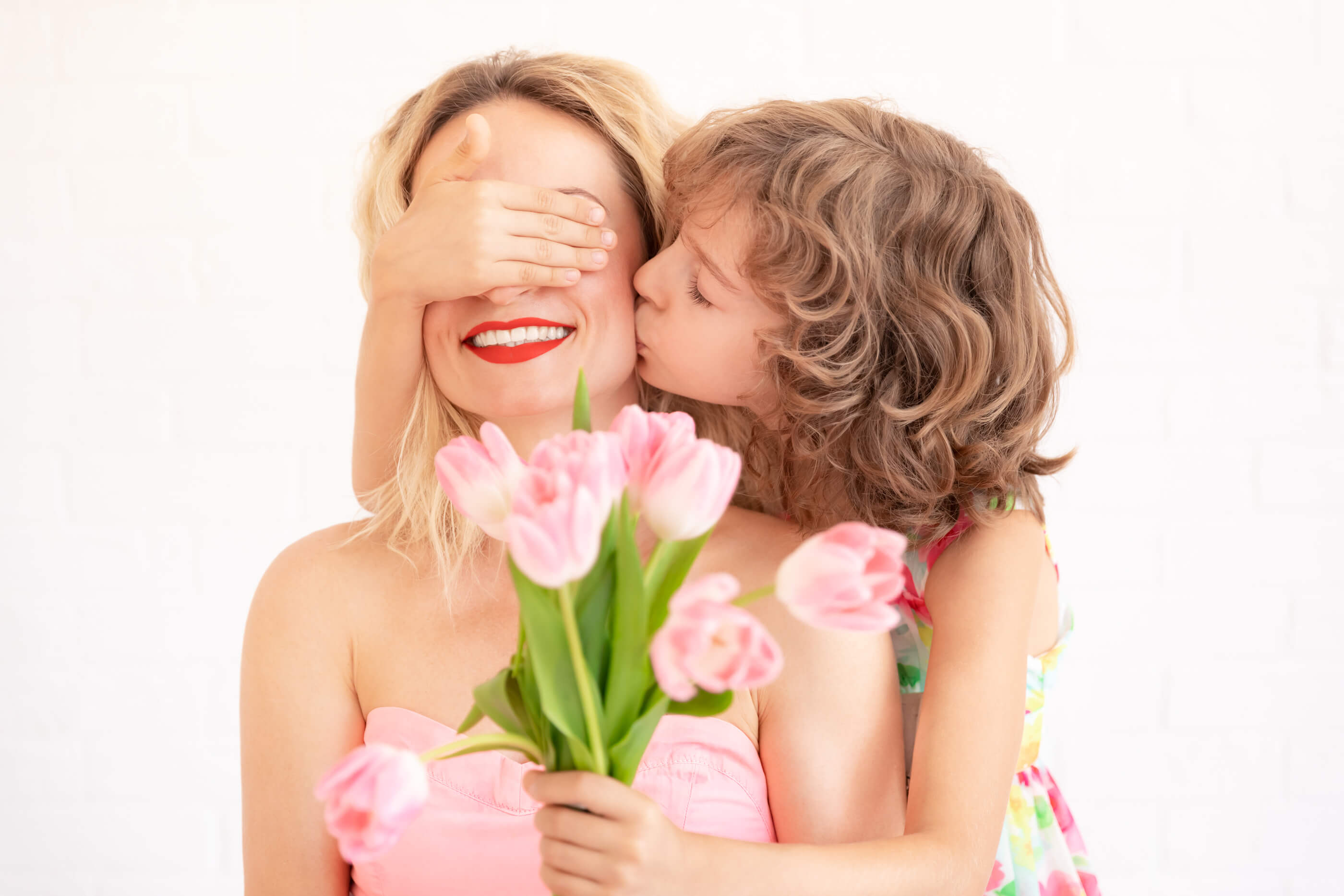 Woman holding pink tulips while a child kisses her cheek