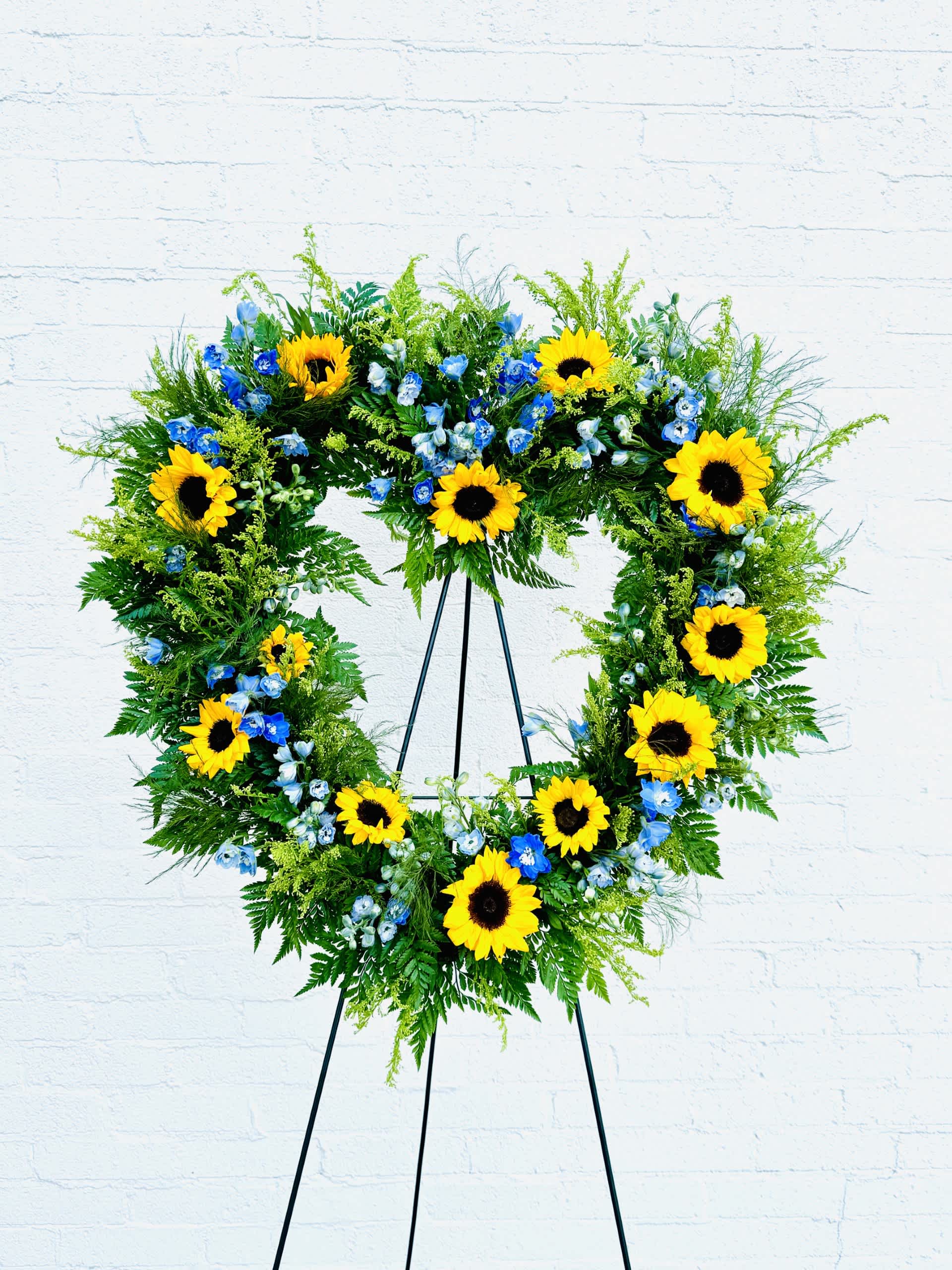 Sunflower Open Heart Sympathy Wreath - This beautiful heart-shaped wreath filled with sunflowers, Solidago and Blue Delphinium is a touching tribute to send for the loved one who enjoyed sunflowers.  Standard 24" x 24"  Heart form including easel for presentation. 