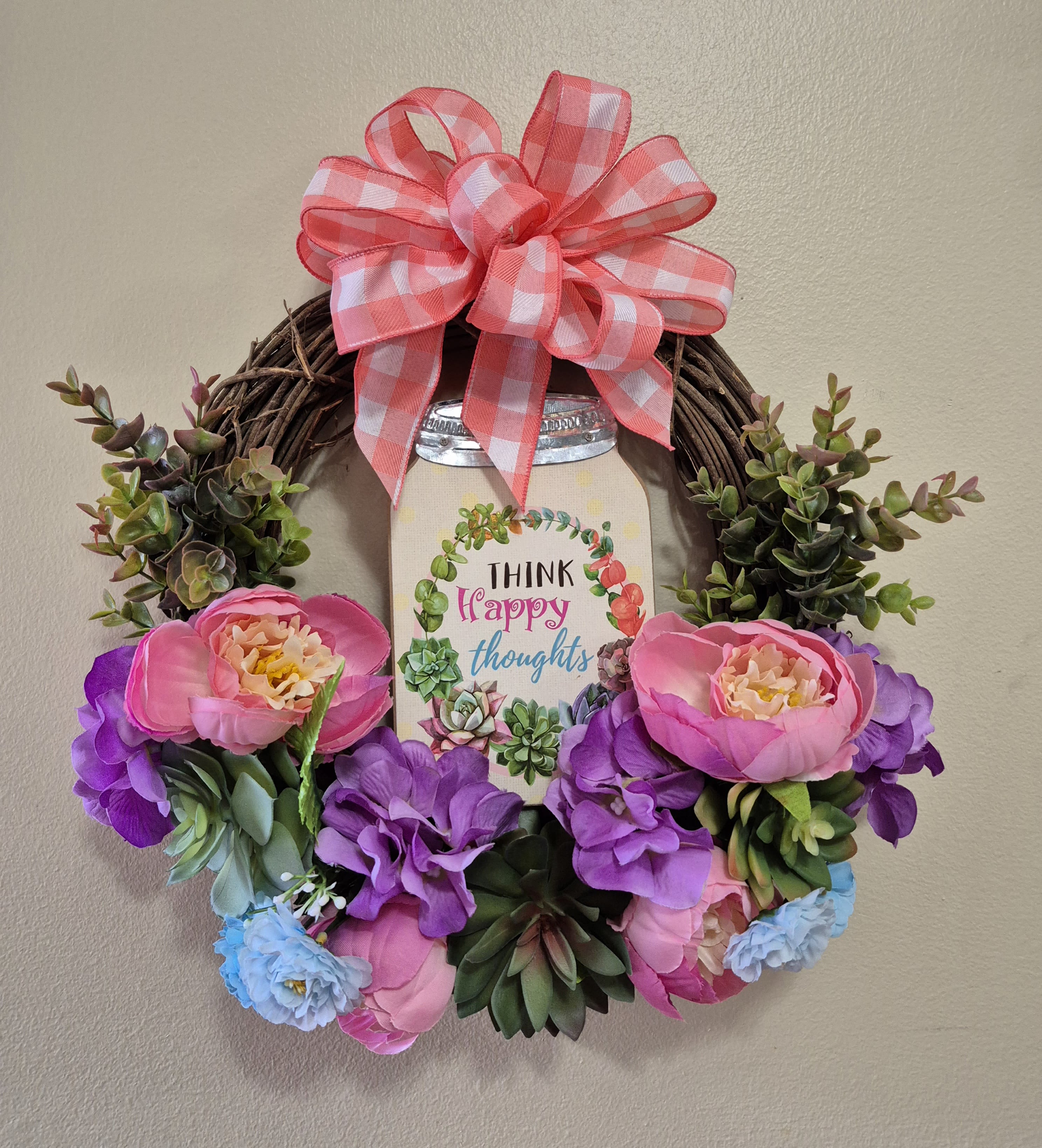 Think Happy Thoughts Silk Wreath -  This "Think Happy Thoughts" silk wreath is sure to make a statement on your front door or send as a gift. Perfect size to send to someone to brighten their day in college, assisted living facility, office etc... Silk pink, purple, light blue flowers and silk succulents. 14" wide all around 