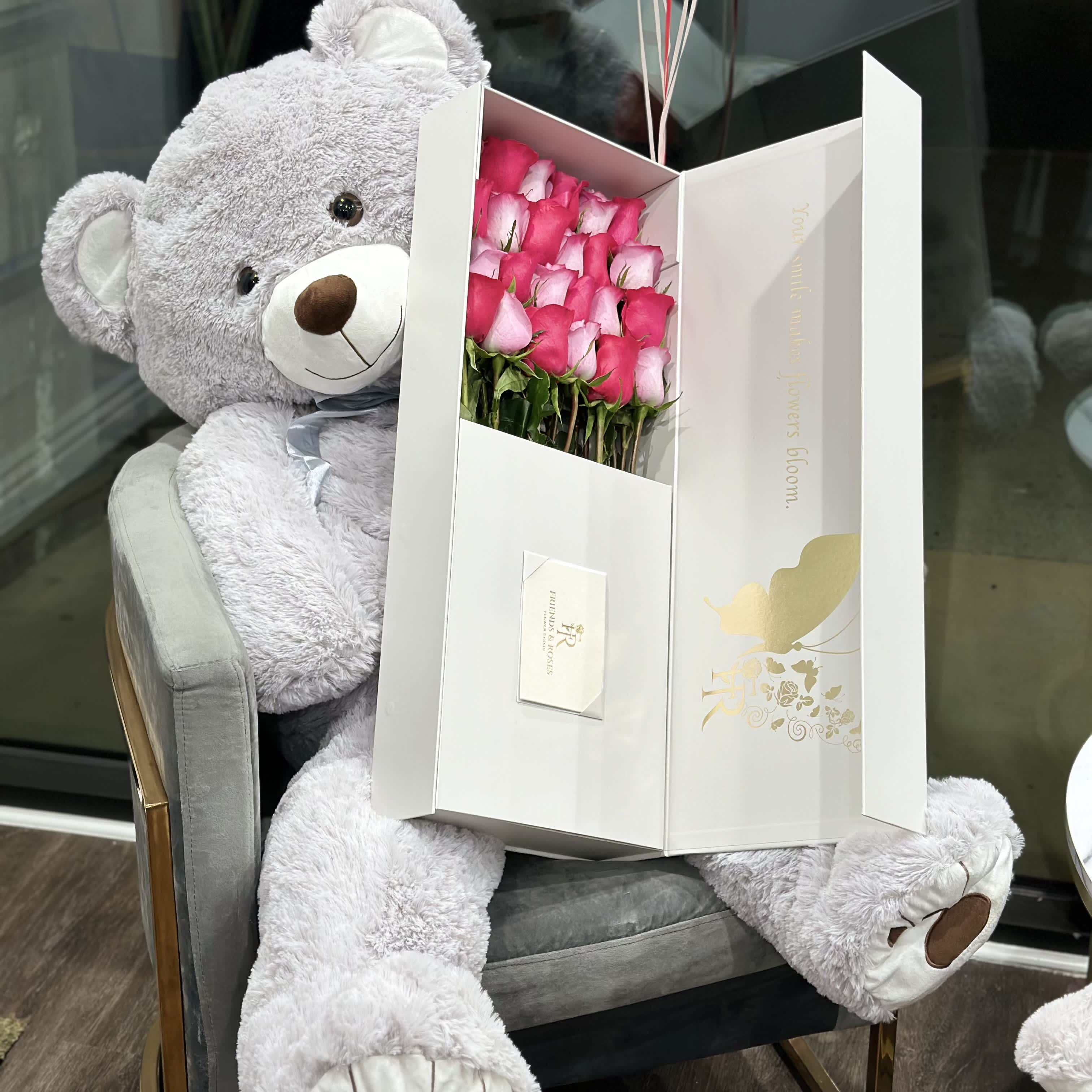 Pink roses in a white gift box beside a large gray teddy bear