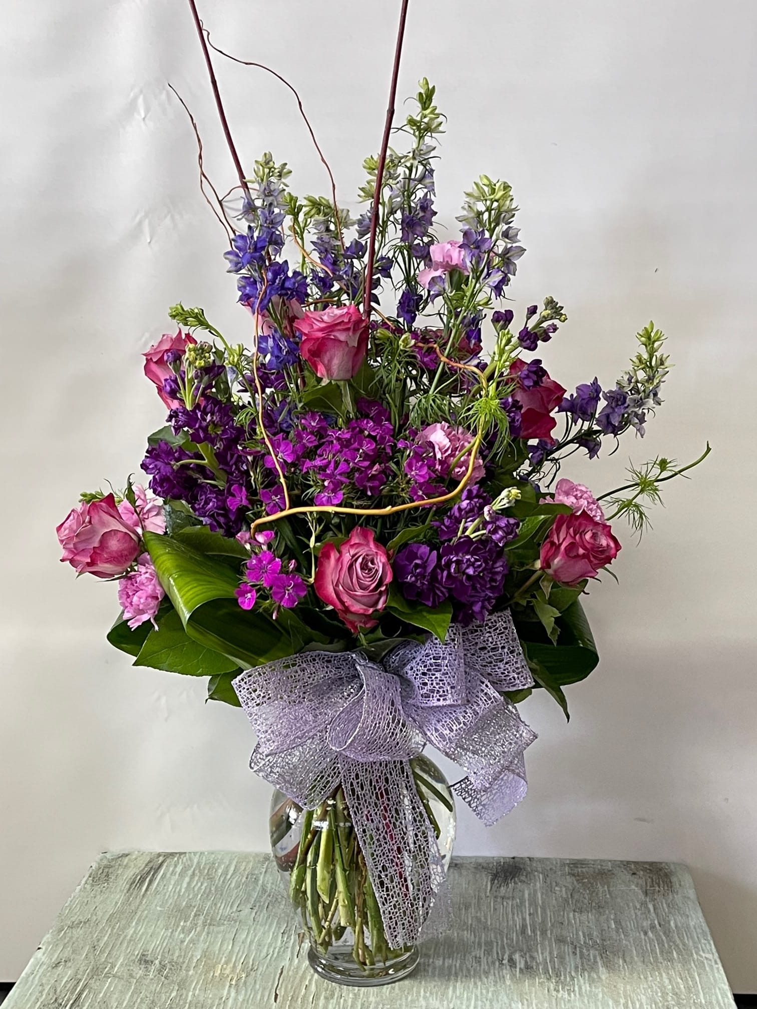 Tall bouquet of pink and purple flowers in a glass vase with a lavender bow