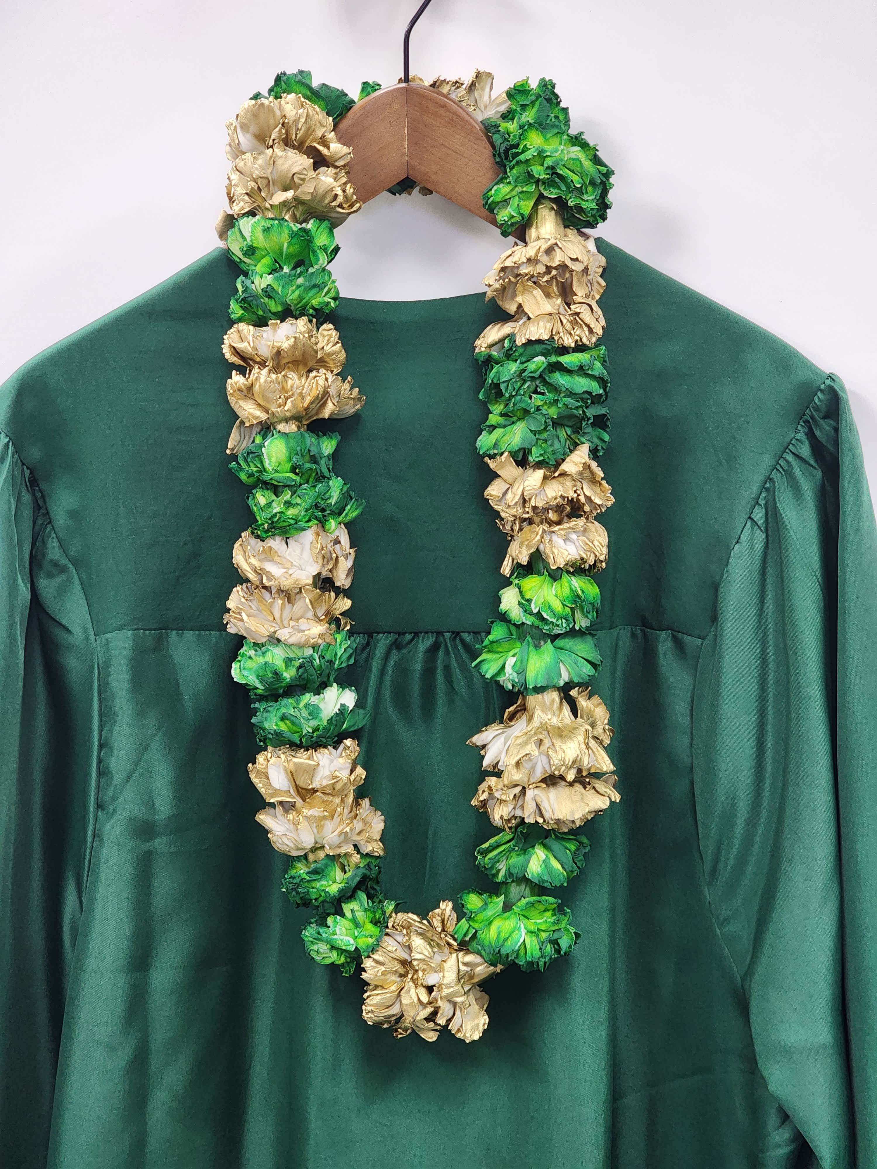 Green and gold floral lei draped over a dark green dress on a hanger