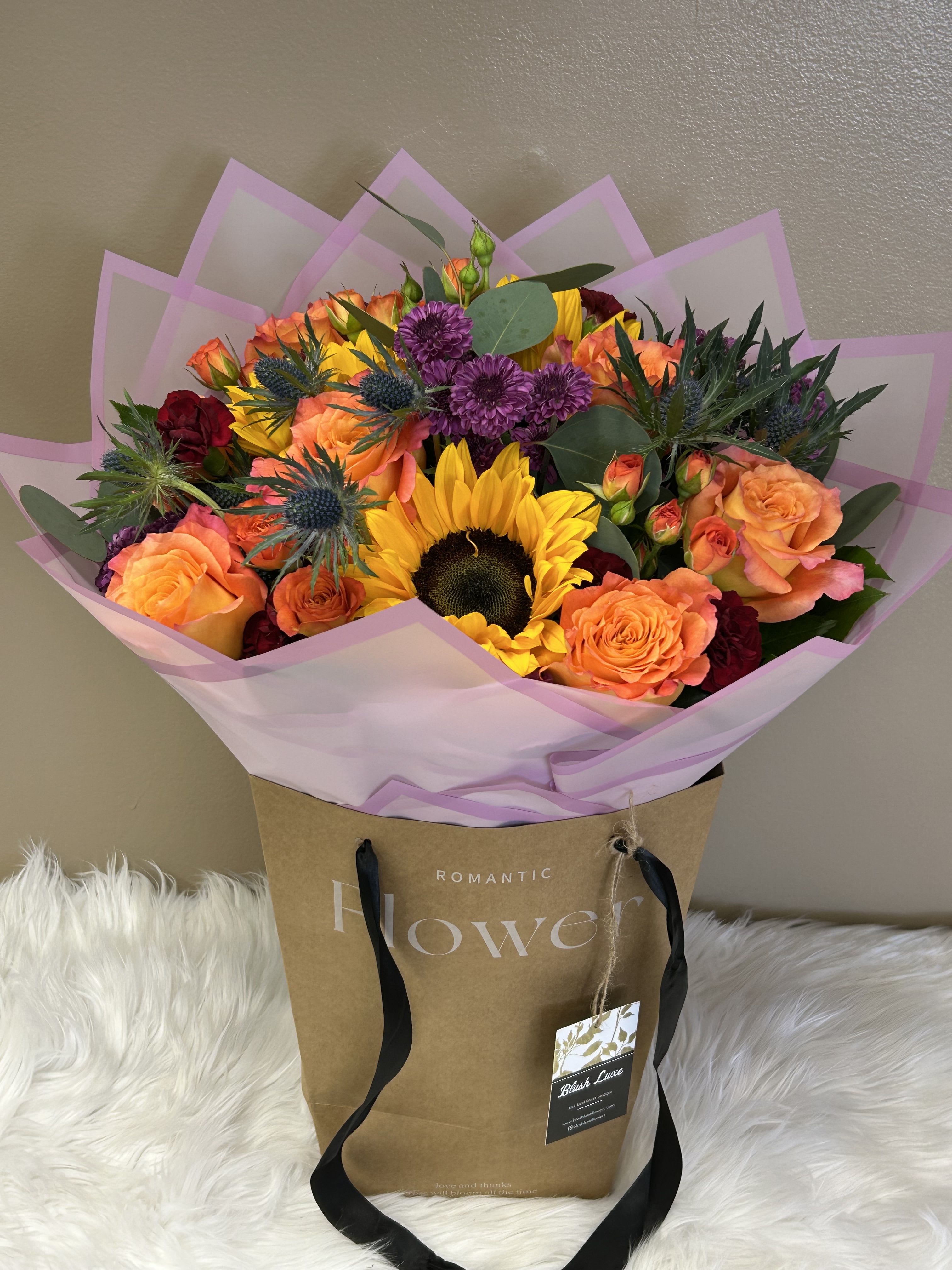 Bouquet of orange roses, sunflowers, and purple blooms in pink wrap