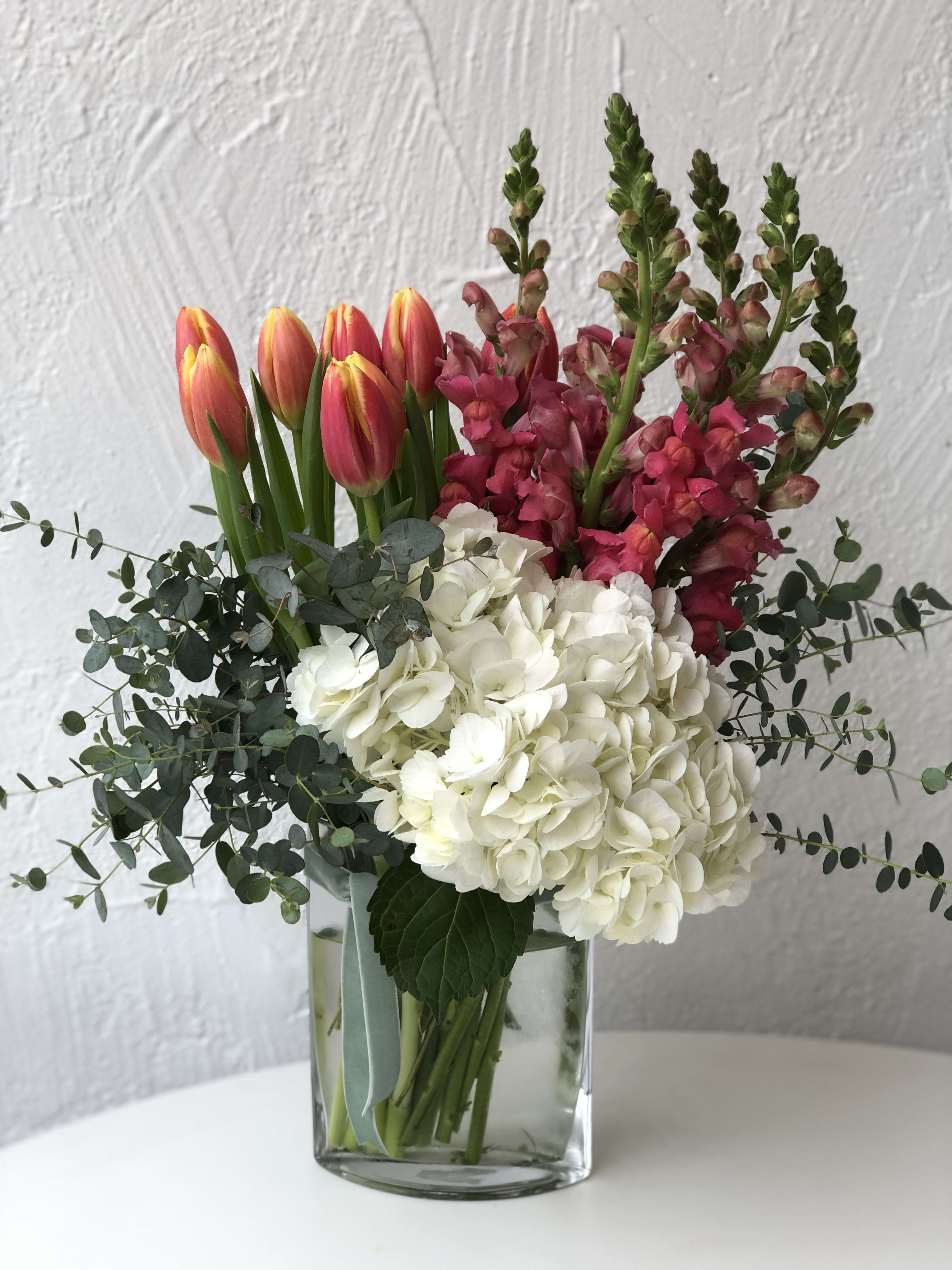 Bouquet of pink tulips, white hydrangeas, and magenta snapdragons in a glass vase