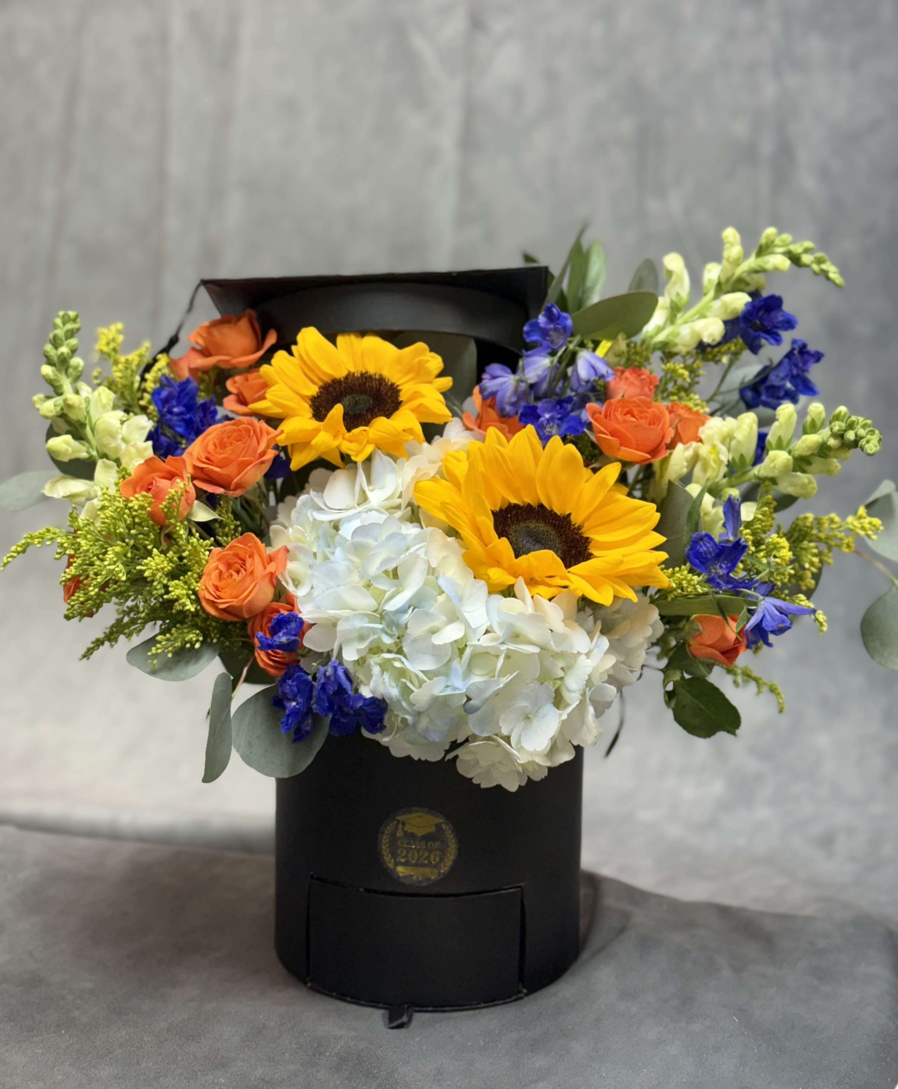 Sunshine &amp; Sweets Grad Box  - Bright, cheerful, and full of sunshine  Our Sunshine &amp; Sweet Grad Box features radiant sunflowers paired with vibrant blooms, arranged in a keepsake graduation box. Finished with a hidden drawer of delicious chocolates, it’s the perfect way to celebrate their big day with a pop of color and sweetness! 