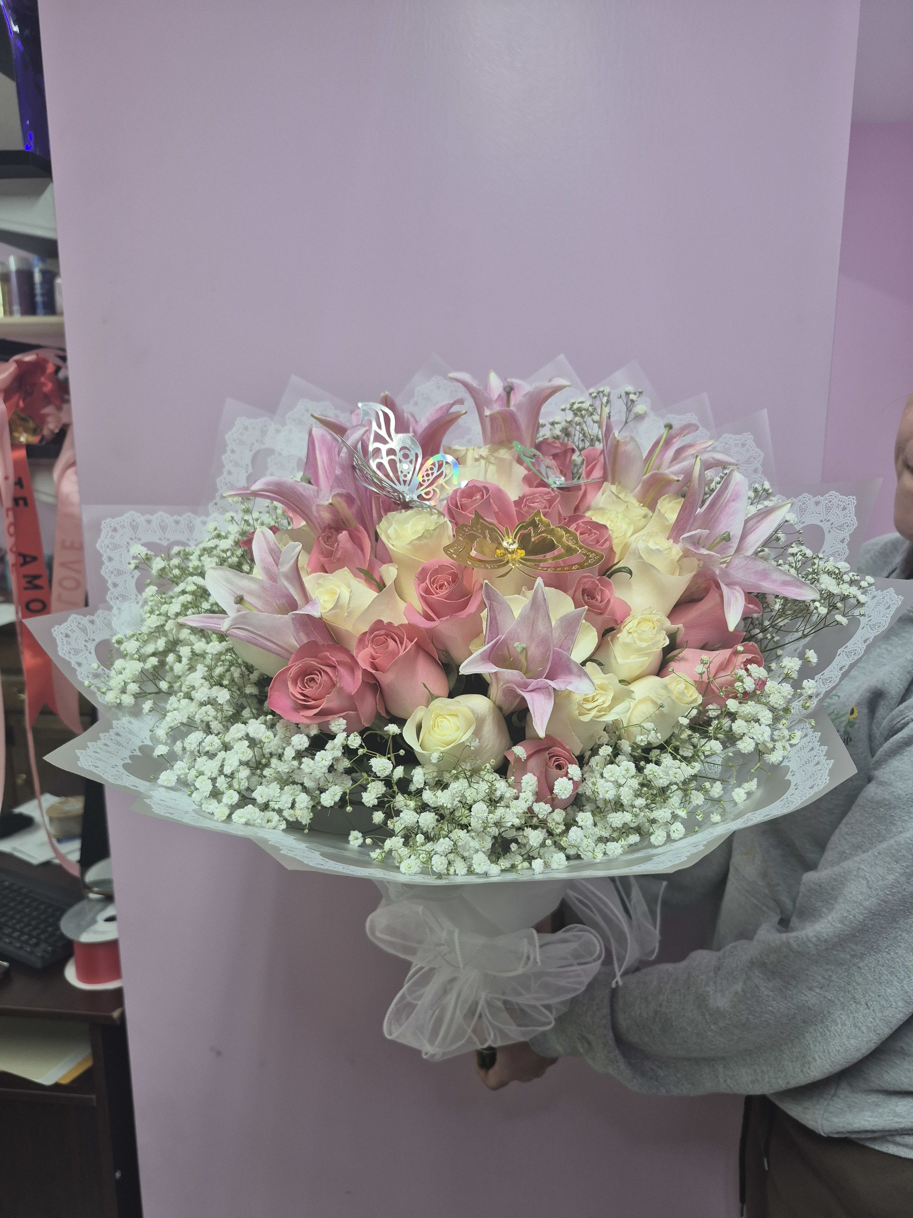 Pink Dreamscape - The Pink Dreamscape arrangement features a stunning collection of soft pink lilies and creamy roses. Delicate white baby's breath surrounds the center flowers to create a full and airy appearance. Decorative butterflies rest among the petals to add a touch of magic and wonder. The bouquet is finished with an elegant white lace wrap and a matching sheer bow. This floral design is a perfect choice for anyone who appreciates grace and a sense of fantasy.