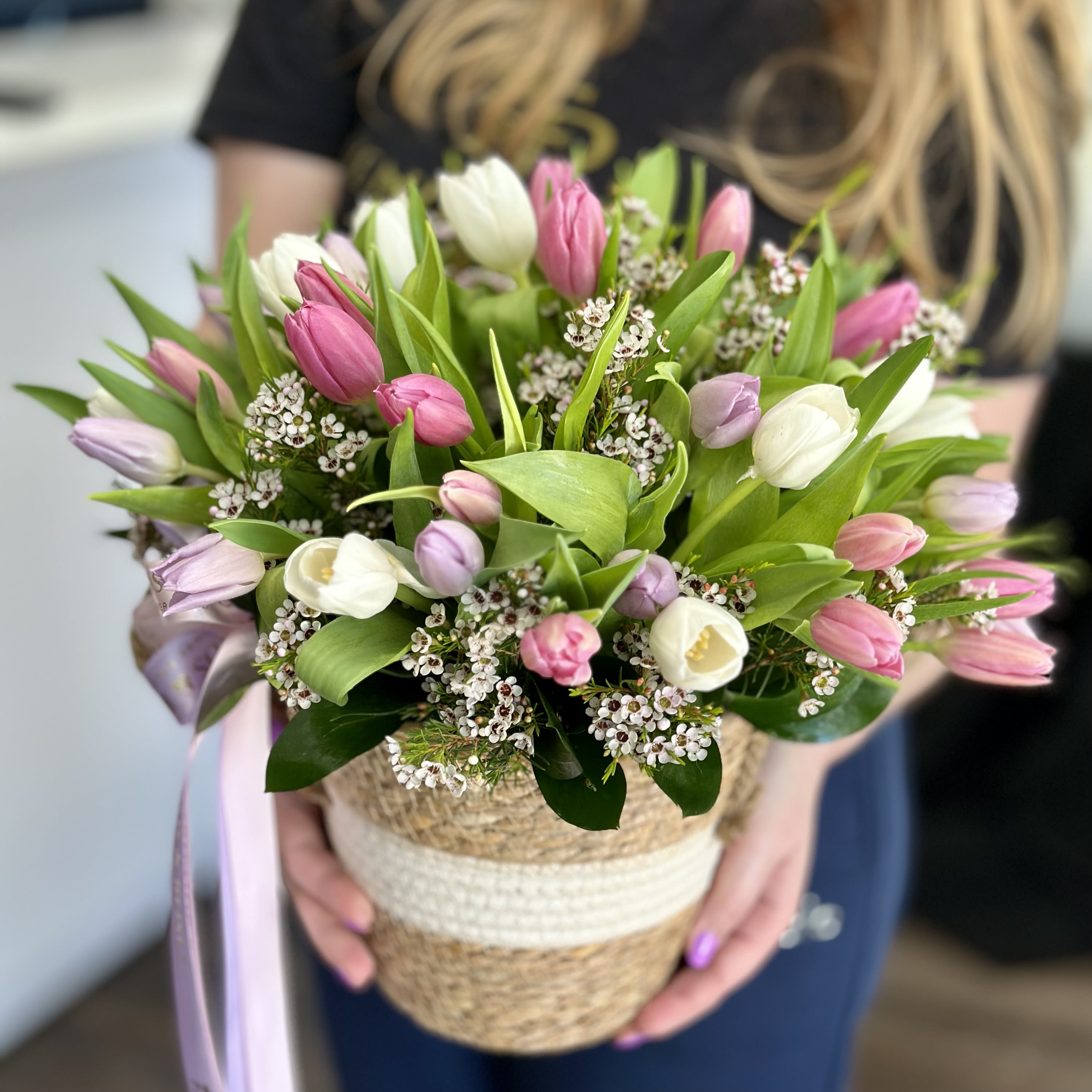 Pink and white tulips arranged in a woven basket with a ribbon