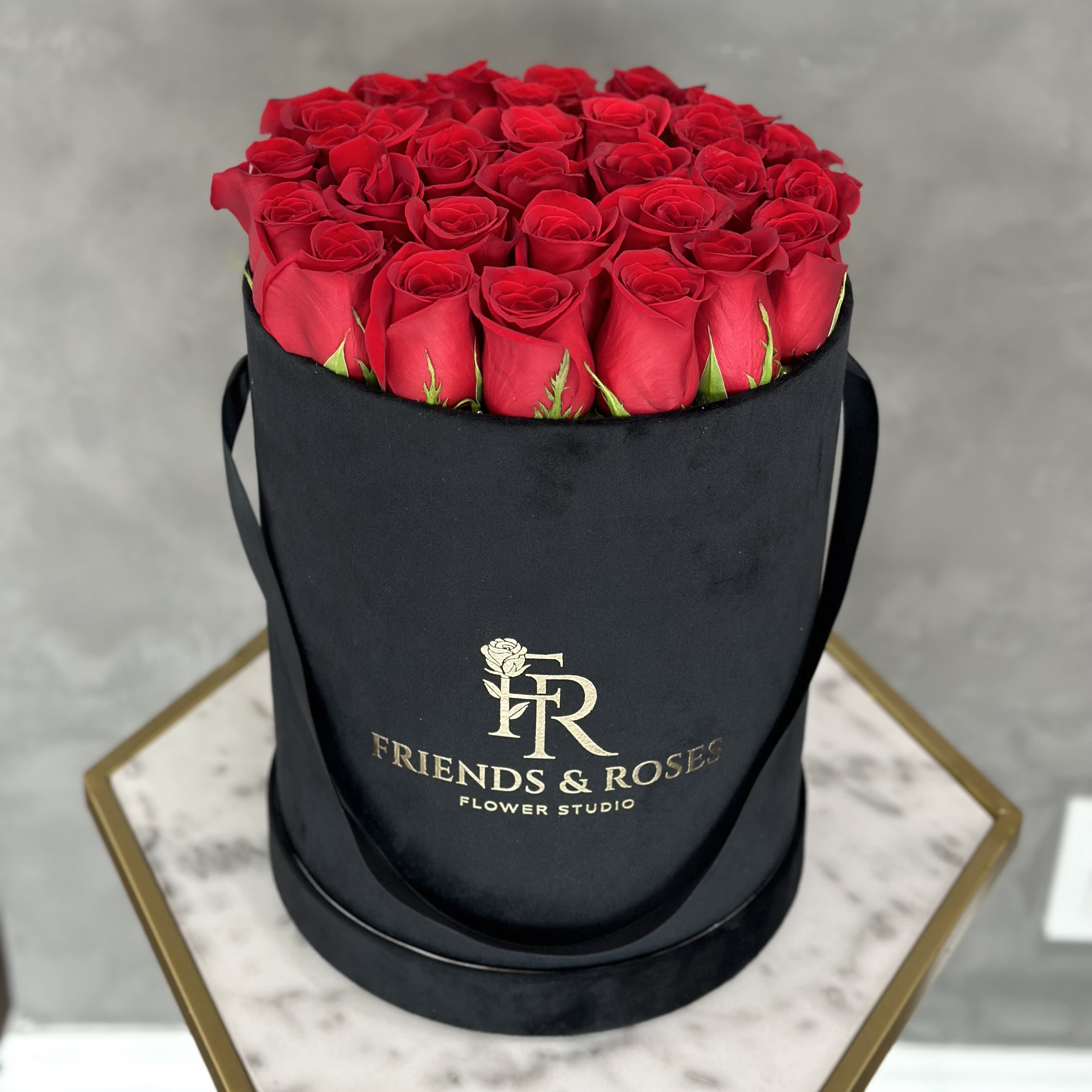 Red roses arranged in a black round hat box with ribbon handles