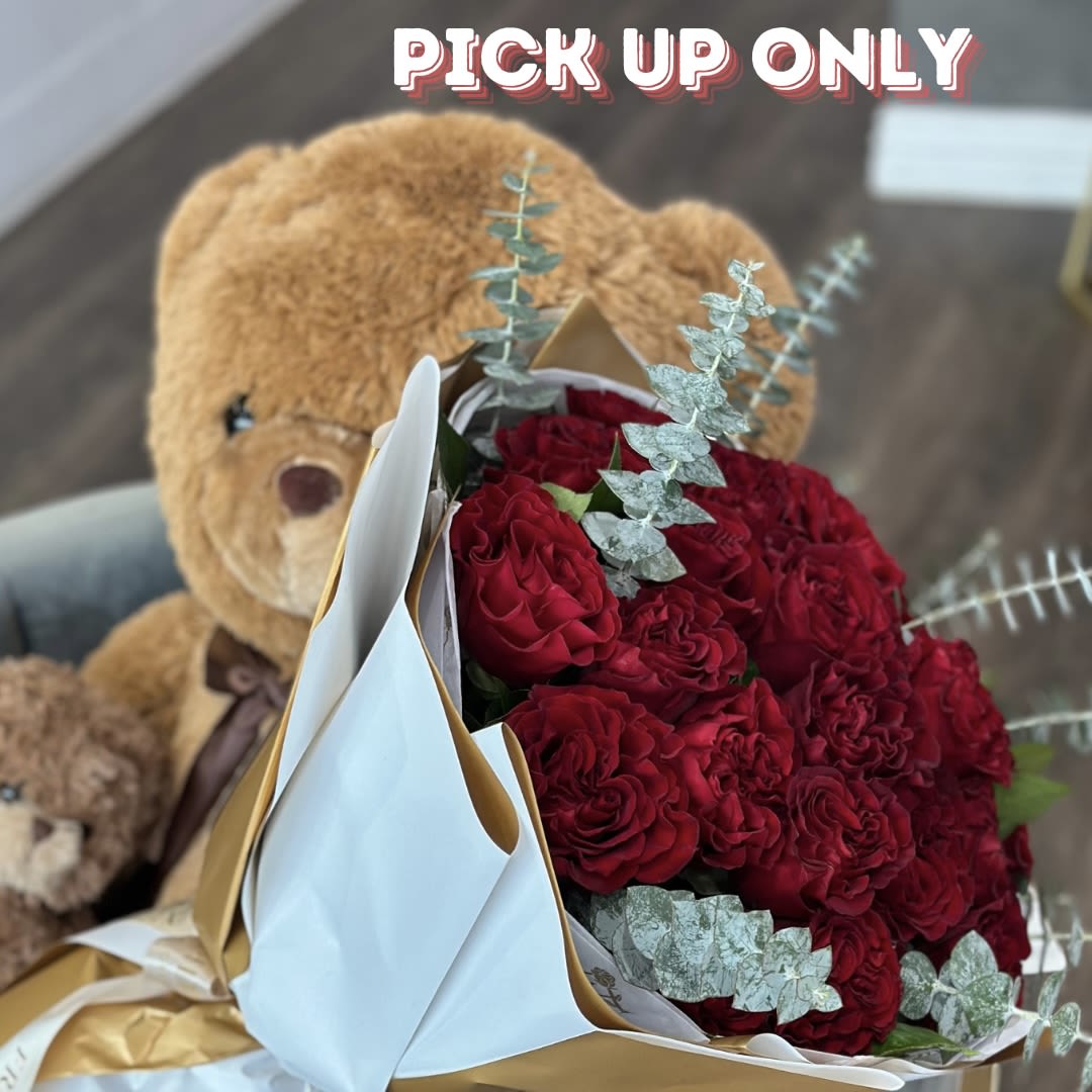 Bouquet of red roses wrapped in white and gold paper with a teddy bear behind it