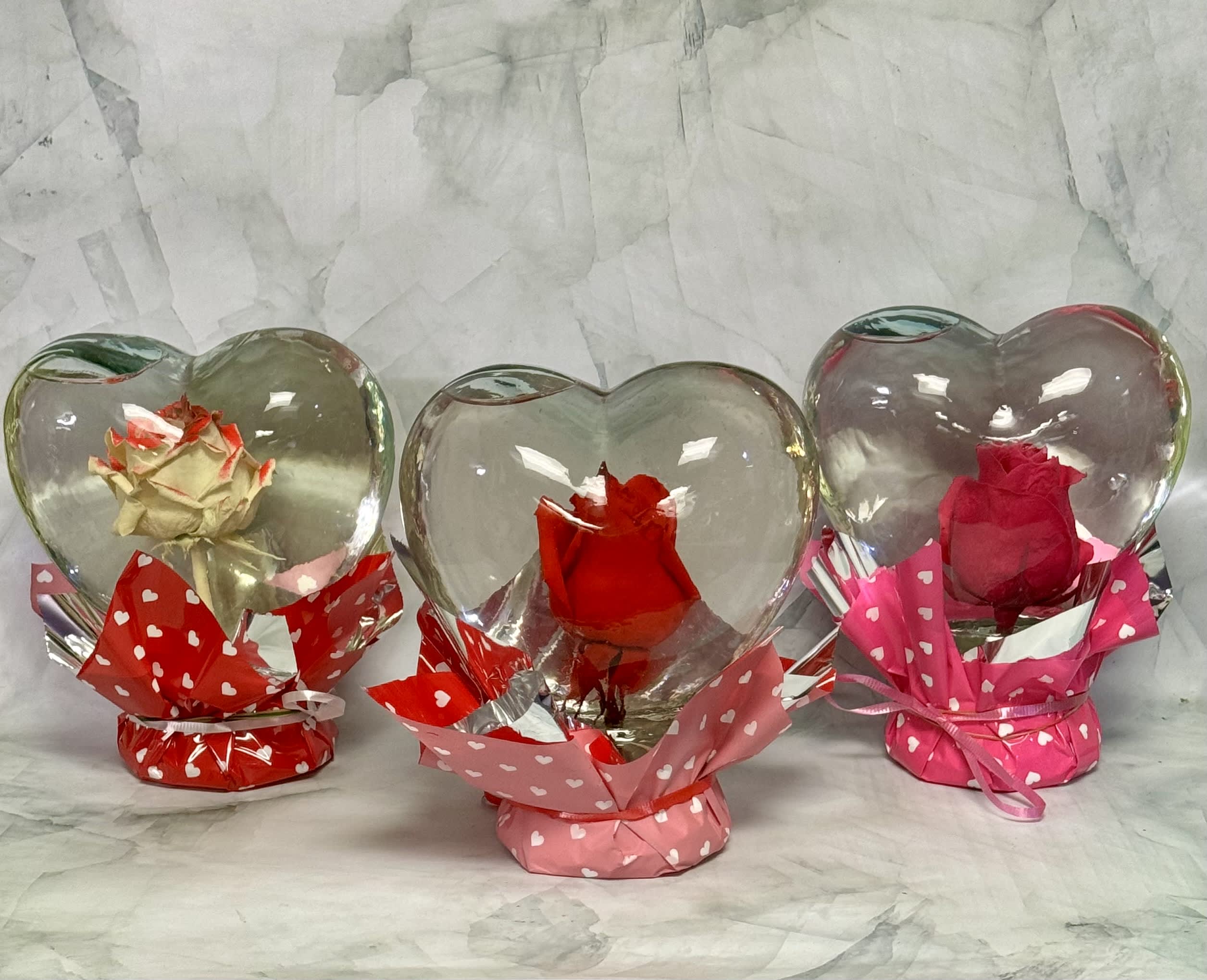 Three roses in heart-shaped glass holders with pink and red wrapping