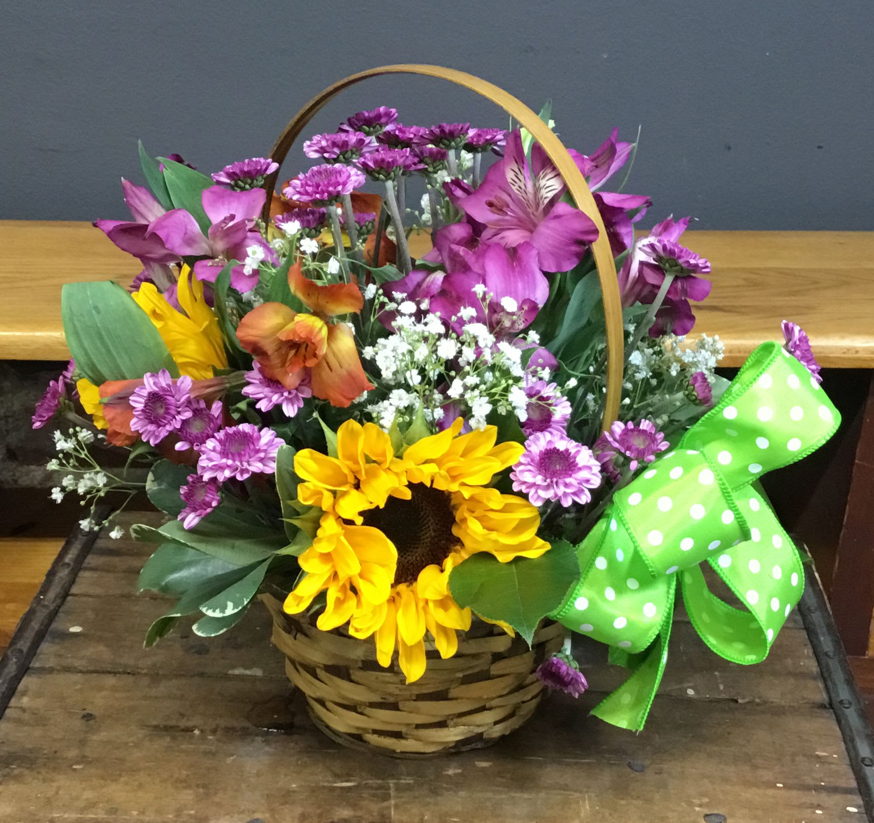 May Day Basket - The woven basket and curved wooden handle give it a homey, hand-tied feel that makes the recipient feel genuinely seen and celebrated from the moment they set eyes on it.  Ideal for brightening a kitchen table, office desk, or bedside, this design arrives ready to display in its woven basket-no vase required. For best results, keep blooms in a cool spot away from direct sunlight and refresh water if you transfer them; the generous mix of stems gives lasting color and cheer throughout the week.