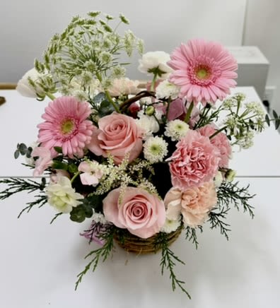 Mother's Day Pink Gerbera Rose Basket - Soft pink gerbera daisies take center stage in this pink and white flower arrangement, making it an ideal birthday bouquet, thank-you gift, or springtime surprise. The Pink Gerbera Rose Basket blends the sunny charm of gerberas with blush roses and ruffled carnations for a romantic, pastel look that will make the person you're thinking of feel warm and celebrated.  A mix of small white filler blooms and airy branching greenery gives the arrangement a loose, garden-style shape while keeping the blooms feeling fresh and light. Flowers are gathered in a low, casual basket for a hand-delivered, homey presentation-cheerful and polished without feeling formal. Perfect for brightening a kitchen table, sending a thoughtful everyday message, or welcoming the season; no special care beyond fresh water and a cool spot will keep the blossoms looking their best for days.