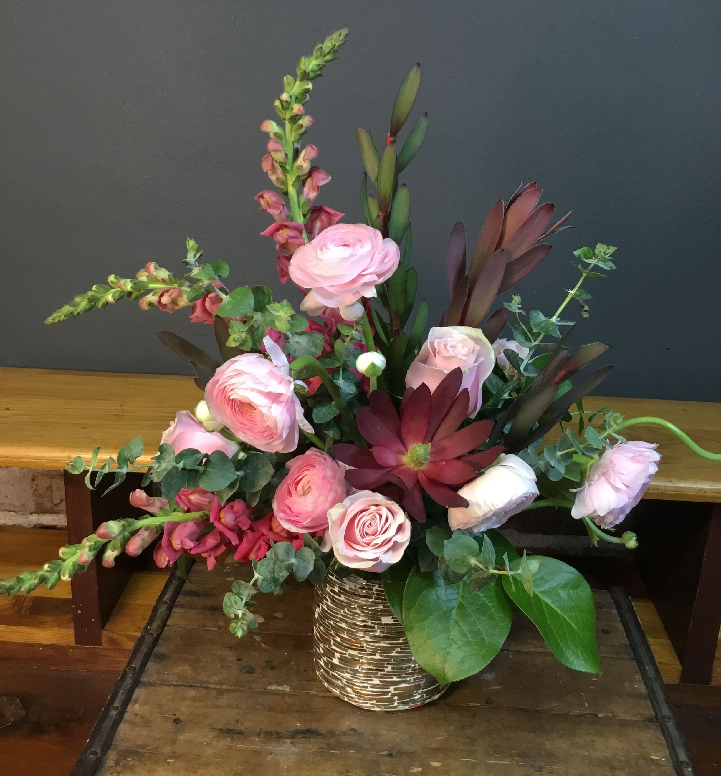 Beautiful - Soft pink roses and delicate ranunculus mingle with tall pink snapdragon spikes and deep burgundy foliage in a romantic garden-style arrangement-perfect as an anniversary bouquet, birthday surprise, or a heartfelt "just because" gift. The loose, asymmetrical design sends blooms outward and upward, giving the recipient a sense of abundance and movement that feels both elegant and effortlessly joyful.  Pale pinks, richer red tones and crisp white accents layer against fresh green leaves for a lush, textured look. Arranged in a small patterned vase, the composition balances soft round blooms with vertical snapdragons for visual contrast and lasting impact. This is the kind of floral gift that makes someone feel truly seen-order sizing and care details at checkout to ensure it arrives ready to enjoy.
