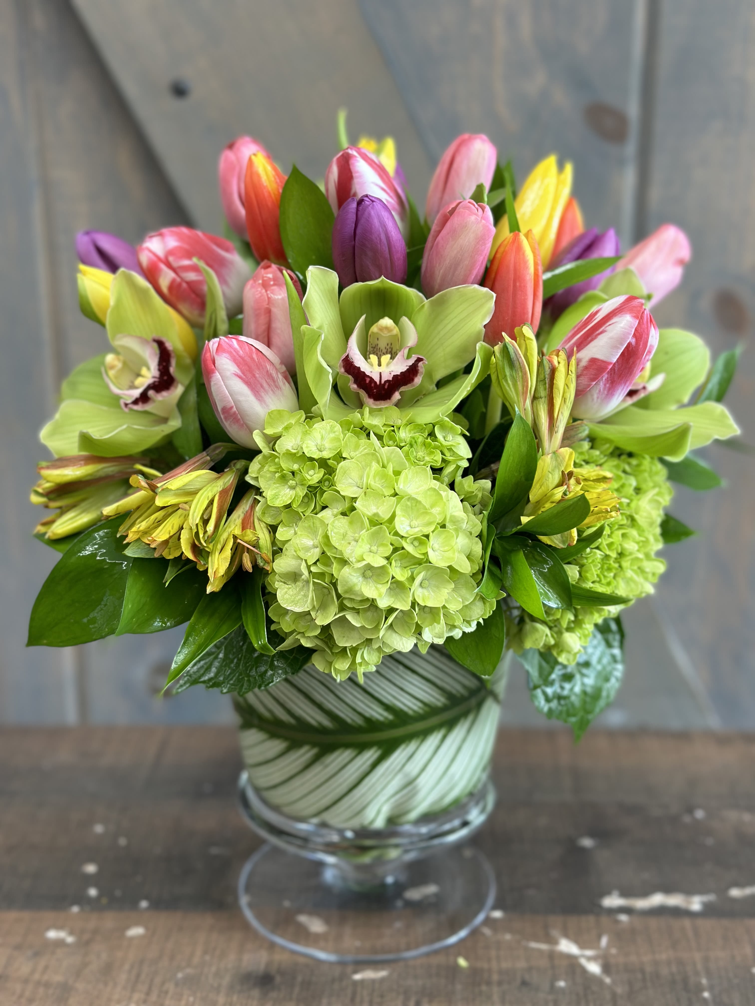 Celebration Tulips - Celebration Tulips is a fun and elegant  arrangement all in one. This design includes Tulips, Hydrangea, Cymbidium Orchids, and Alstroemeria within a glass pedestal vase lined with a tropical leaf.