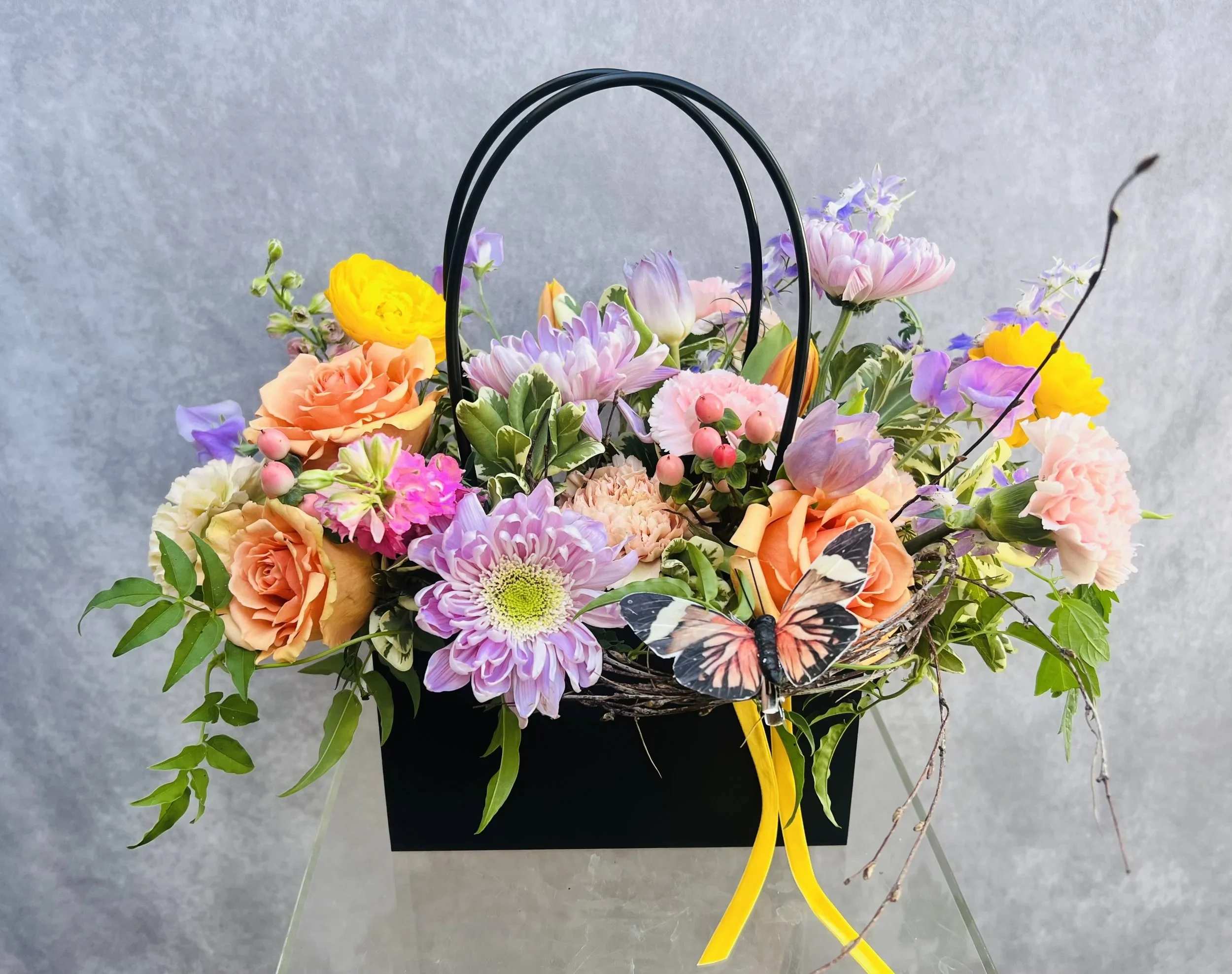 Charlotte - This pastel floral arrangement is designed to feel soft, fresh, and effortlessly beautiful. Created with premium seasonal blooms and lush greenery, each piece is thoughtfully handcrafted to highlight natural color, texture, and movement.  Arranged in a reusable keepsake kraft tote bag, this design blends style and function, making it a unique and lasting gift. The soft pastel palette brings a light, uplifting feel that works beautifully for a variety of occasions, from birthdays to thank-yous or simply brightening someone’s day.  Available in three tote color options—black, white, and pink—each arrangement offers a slightly different look while maintaining the same refined, garden-inspired style.  Flowers and greenery may vary due to seasonal availability, but that’s part of the charm! Our creative designers will substitute with the freshest high end product available- some grown in our very own garden!- and create something beautiful.  *Have a special request?* Let us know in the special instructions section during checkout.
