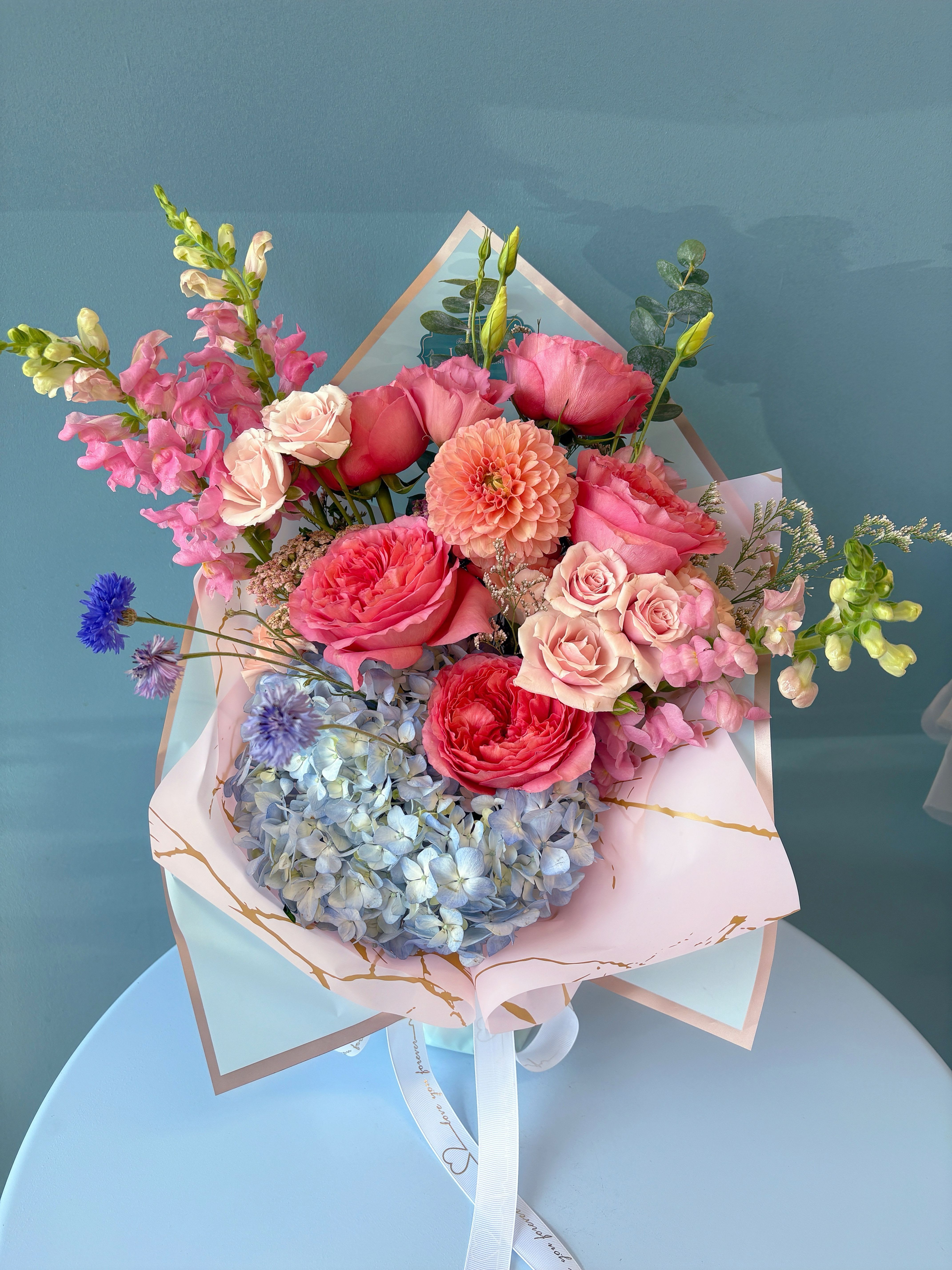 Bouquet of pink roses, hydrangea, and snapdragons in pastel wrapping