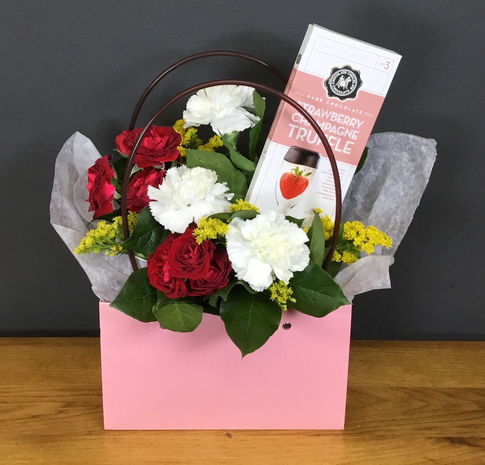 Berry Best Mom Gift Bag - Fresh flowers, greens and filler flowers make this Berry Best Mom Gift Bag a cheerful flower arrangement for Mother's Day, birthdays, anniversaries, or Valentine's Day. Nestled in a gift bag with a brown handle and tissue paper, the compact hand-gift format reads as both romantic and celebratory-perfect for the mom who deserves something sweet and stylish.  Give this to the mom who loves a little glamour and sweetness; she'll feel seen and celebrated the moment she opens the bag. Order for same-day pickup or local delivery to make sure the flowers and chocolate arrive fresh-tissue-lined and ready to present.