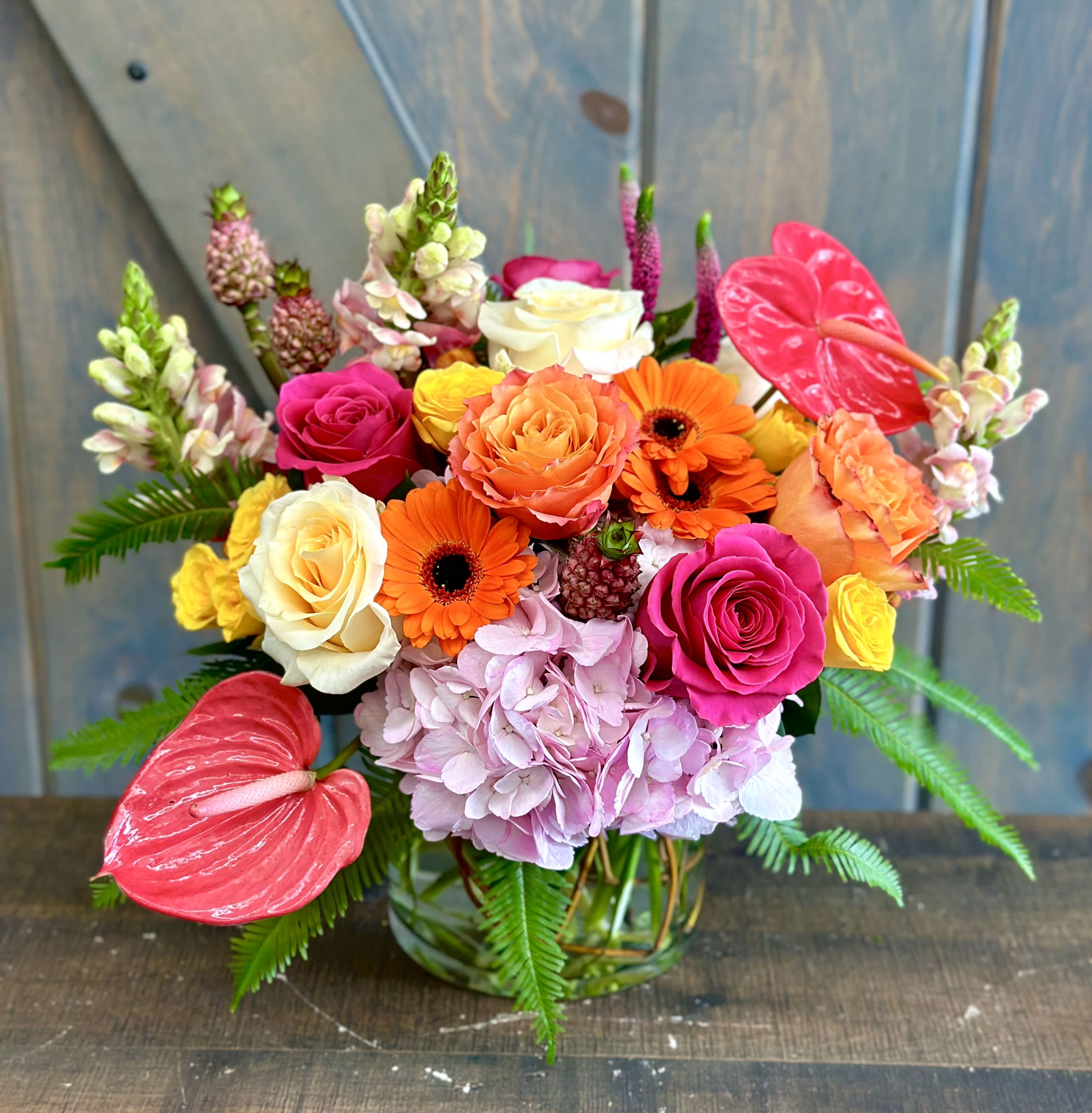 Pineapple Express - All aboard this tropical and fun arrangement, and yes there are actual mini Pineapples included. Other florals in this design are Hydrangea, Roses, Spray Roses, Gerbera Daisies, Snap Dragons, Veronica, Anthurium, and umbrella fern