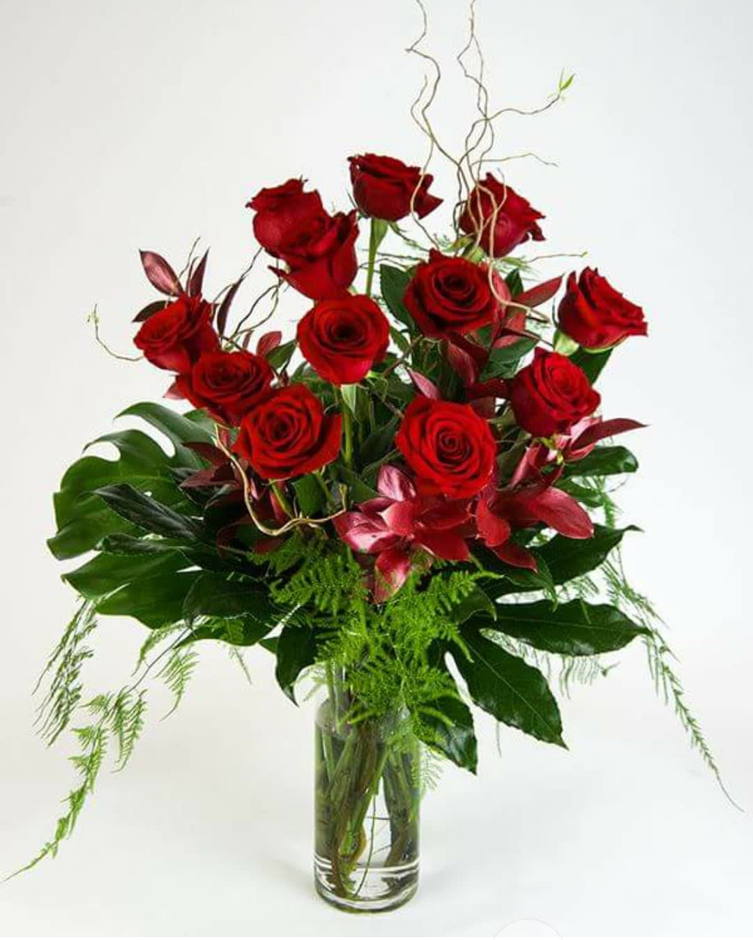 Red roses arranged in a clear glass vase with tropical foliage