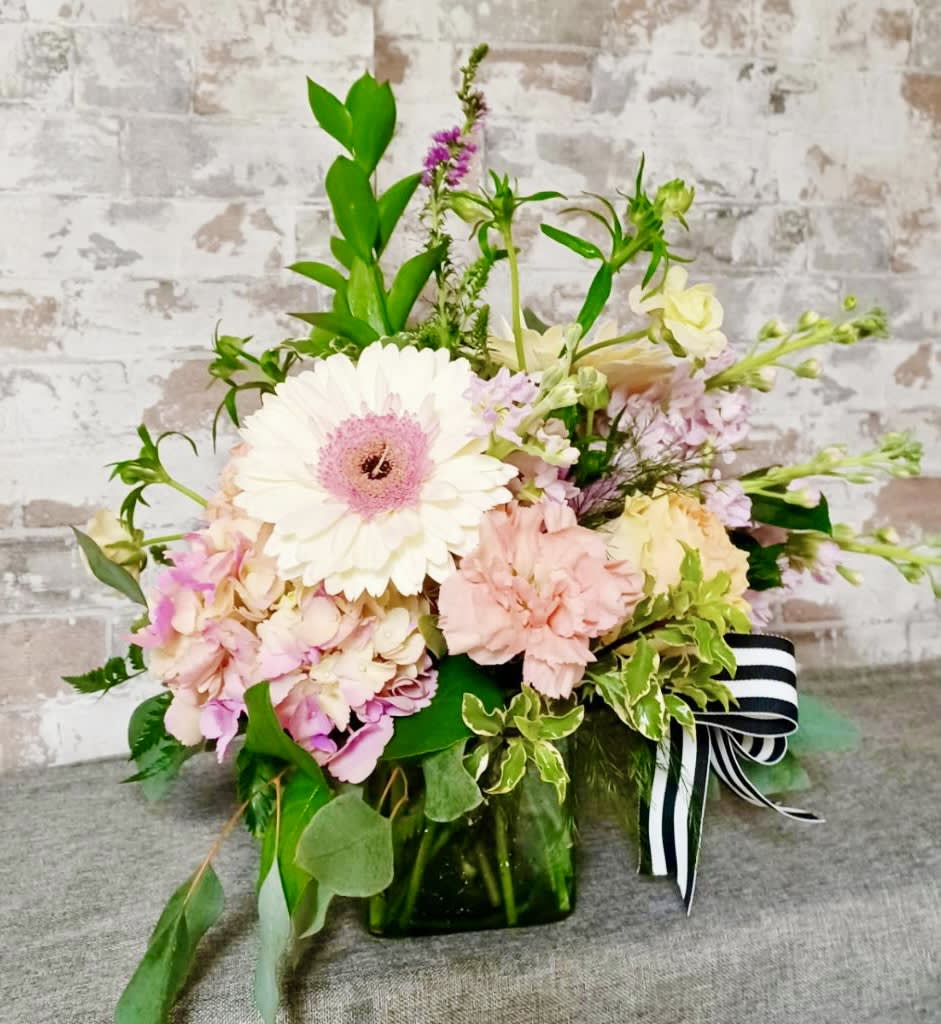 Pastel flower arrangement in a green glass vase with a striped ribbon