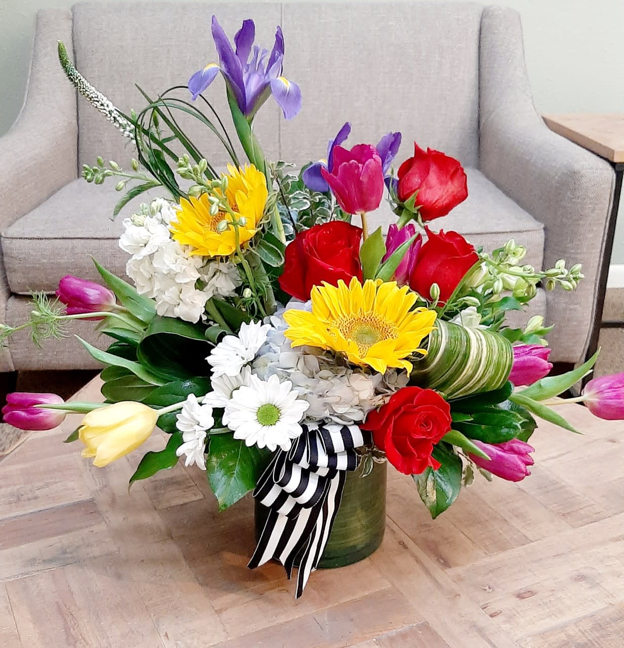 Colorful mixed flower arrangement in a green vase with a striped ribbon
